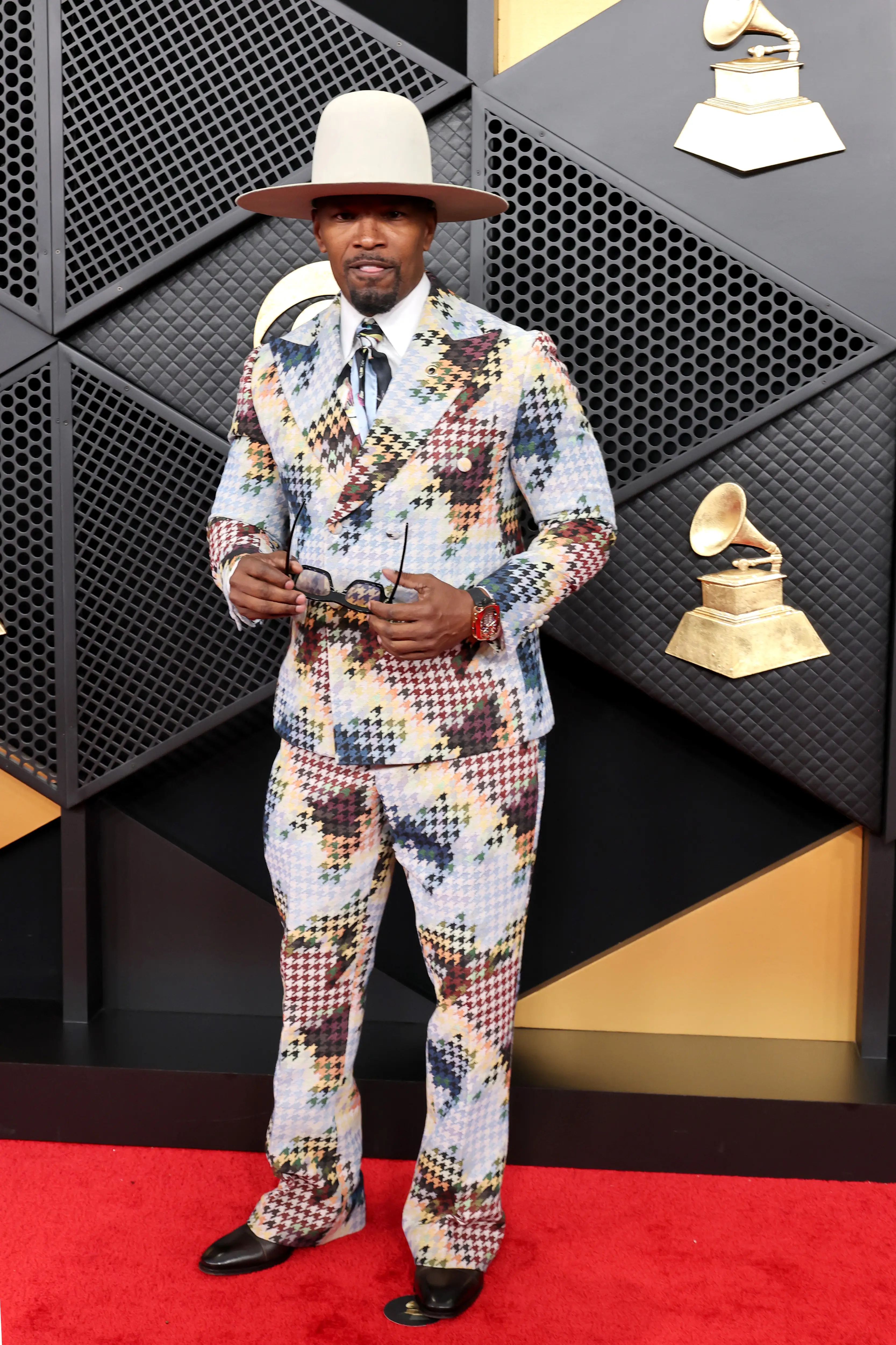 Jamie Foxx walks the 2026 Grammy Awards red carpet in a colorful suit and tan hat.