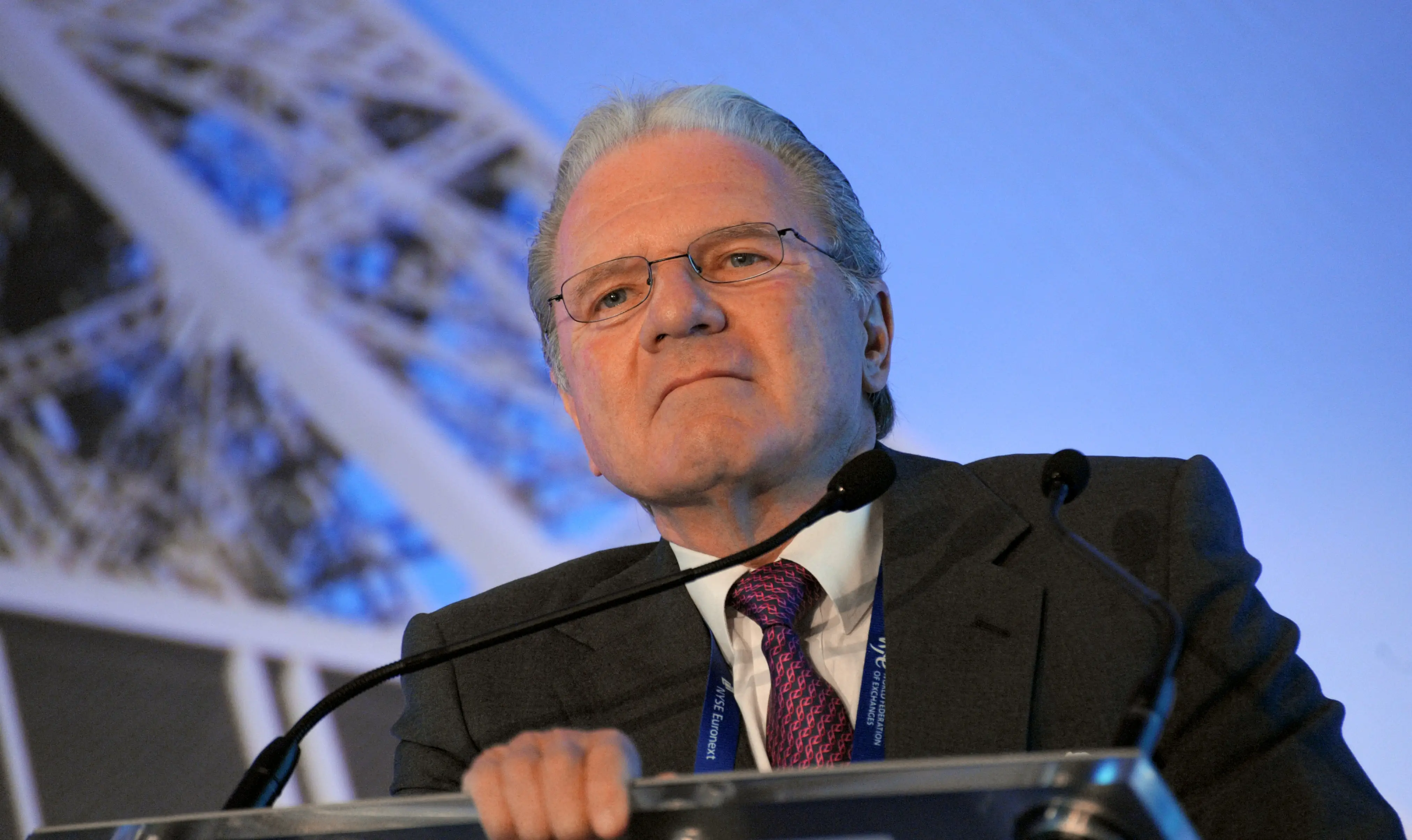 Thomas Peterffy, a gray-haired man in a suit and glasses, photographed from below at a podium.