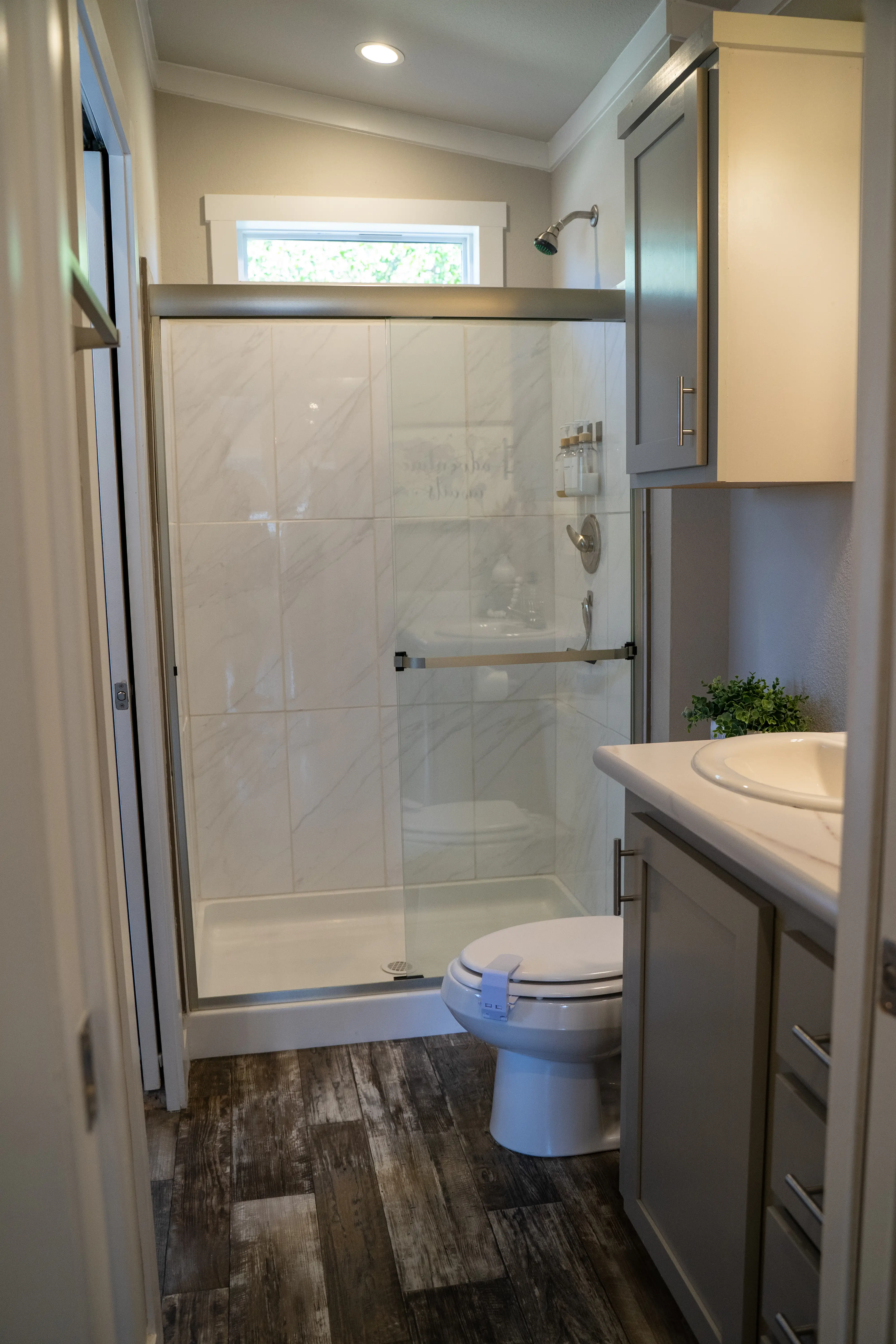 A full size bathroom, which includes a standing shower, toilet, and sink, in a tiny home.