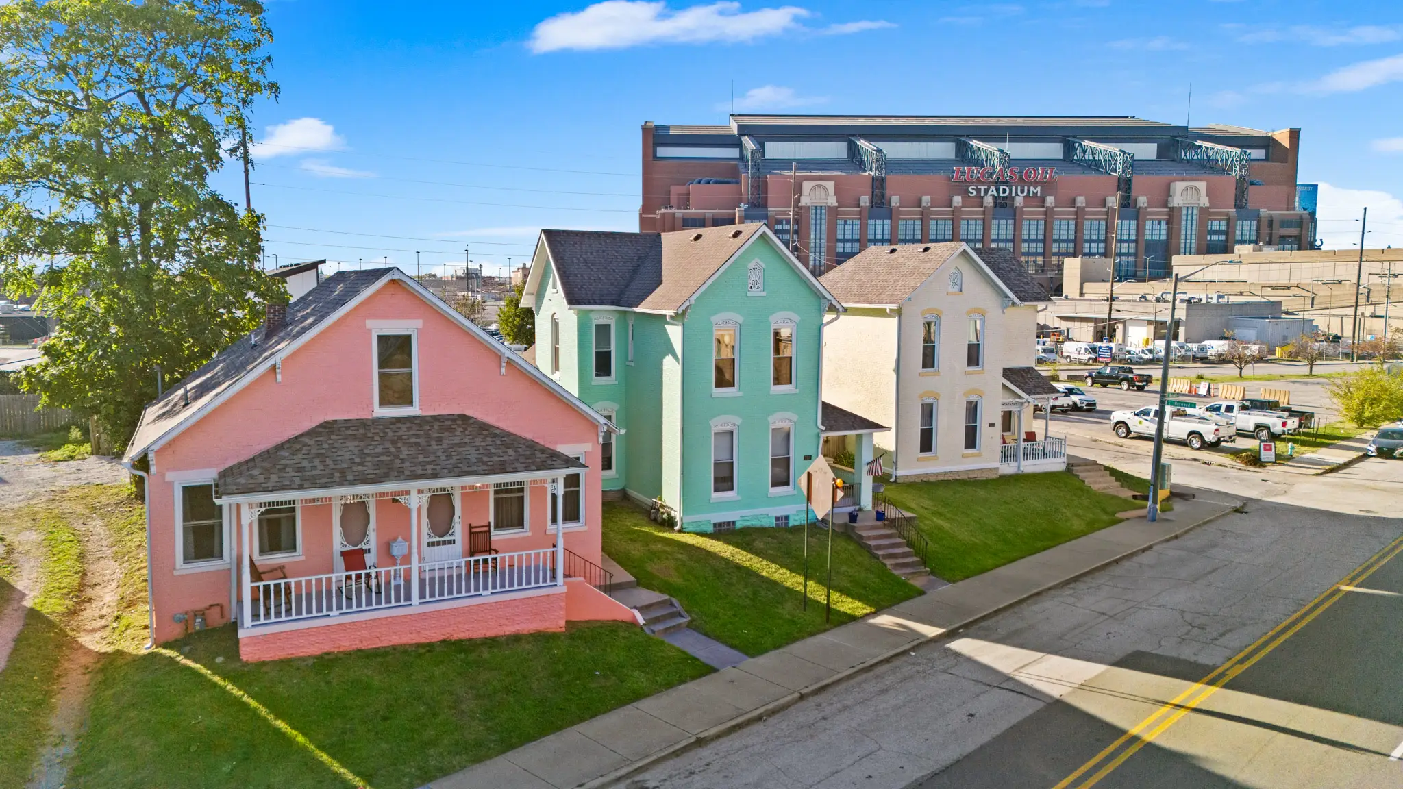 Brightly colored rental homes in pink, sea foam green, and yellow, with Lucas Oil Stadium in Indianapolis, Indiana, in the background.