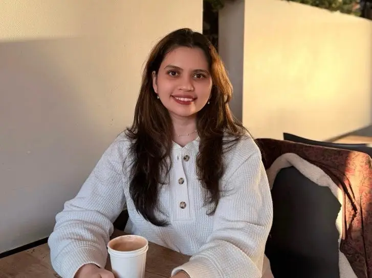 a woman poses with a coffee at a table