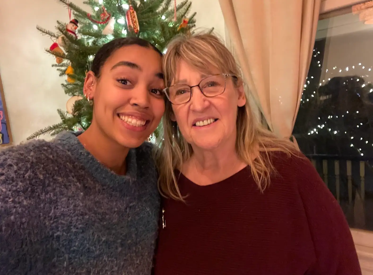 The writer and her grandmother posing in sweaters in front of a Christmas tree.