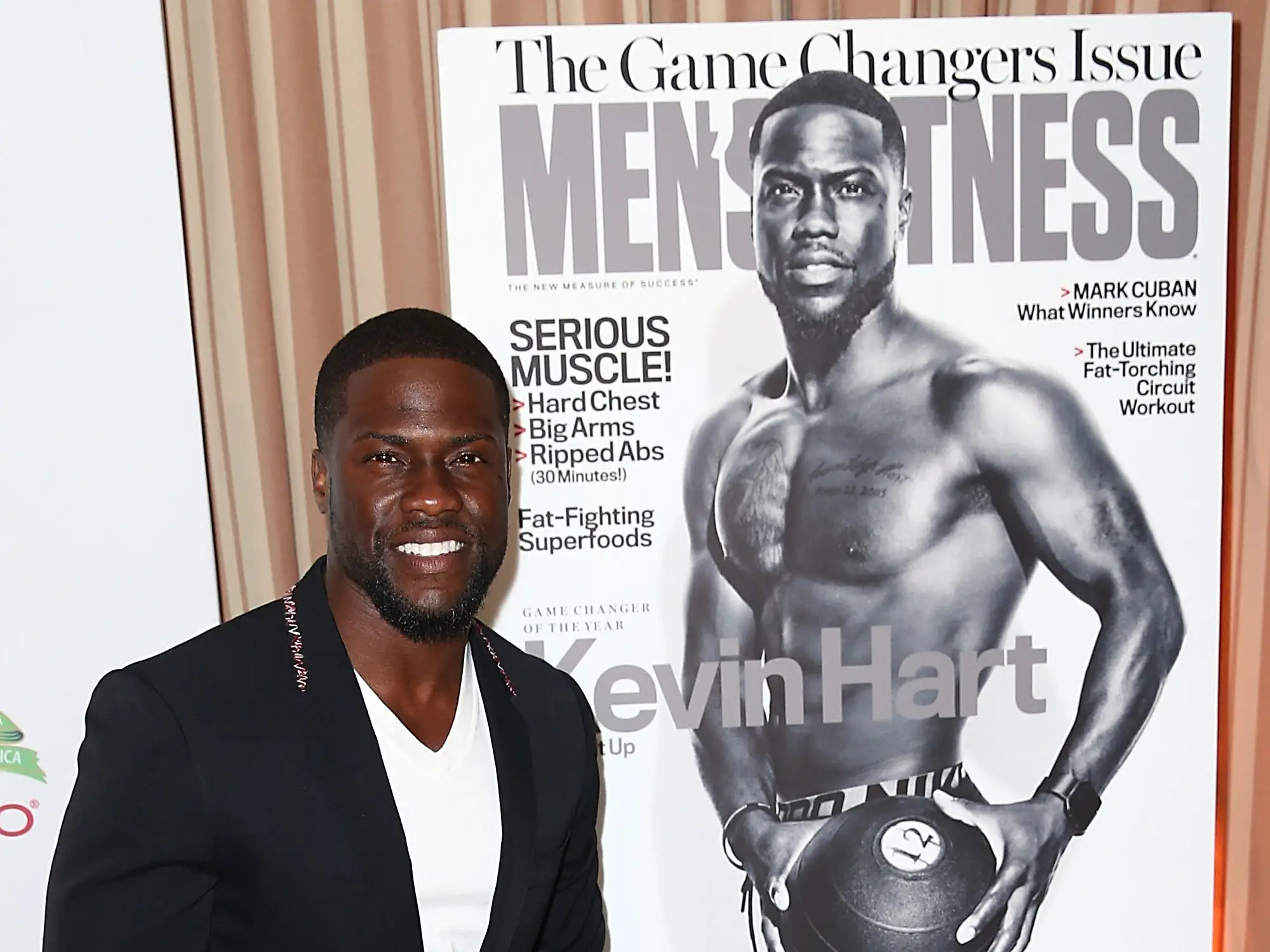 Kevin Hart posing next to his cover issue of Men's Fitness