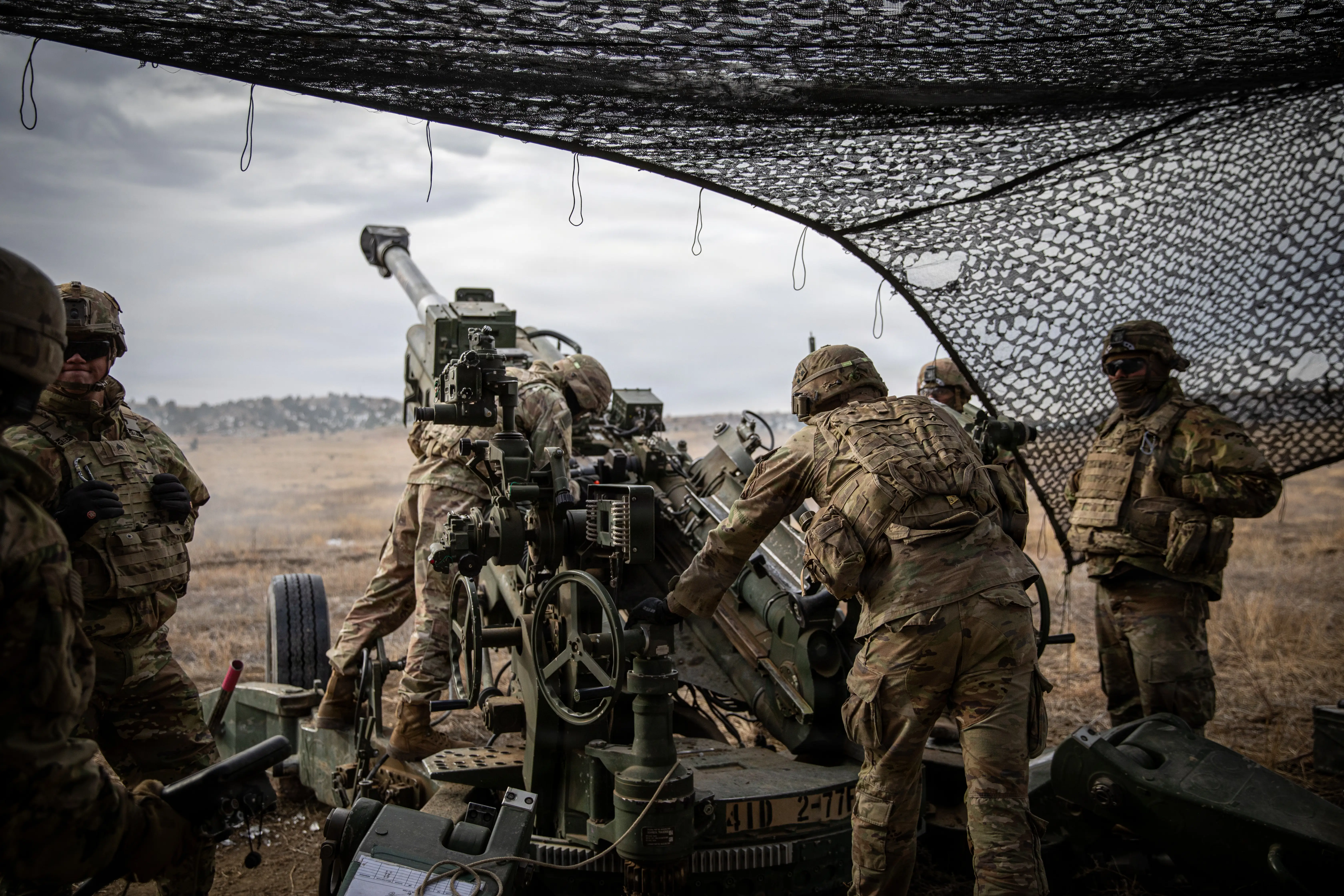 Soldiers stand around an artillery piece preparing to fire it in a field.