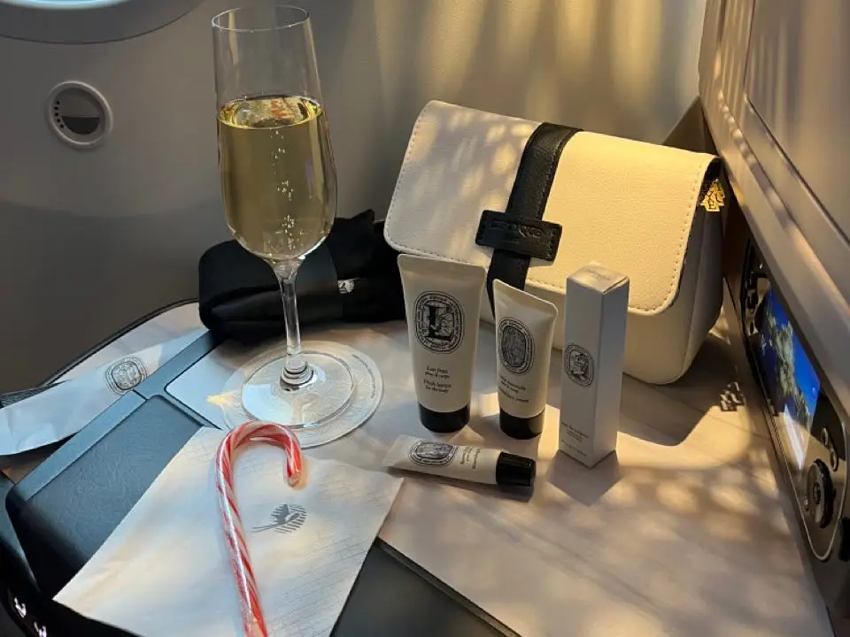 Toiletries, champagne, and toiletry bag on tray table on Qatar Airways flight