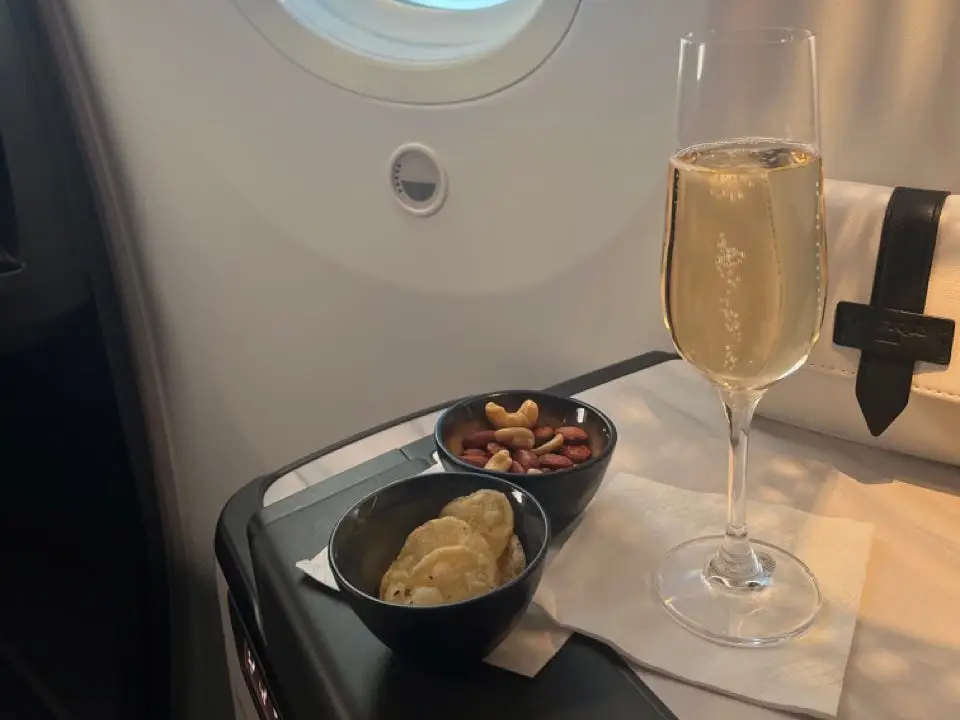 Champagne next to bowls of crisps and nuts next to plane window