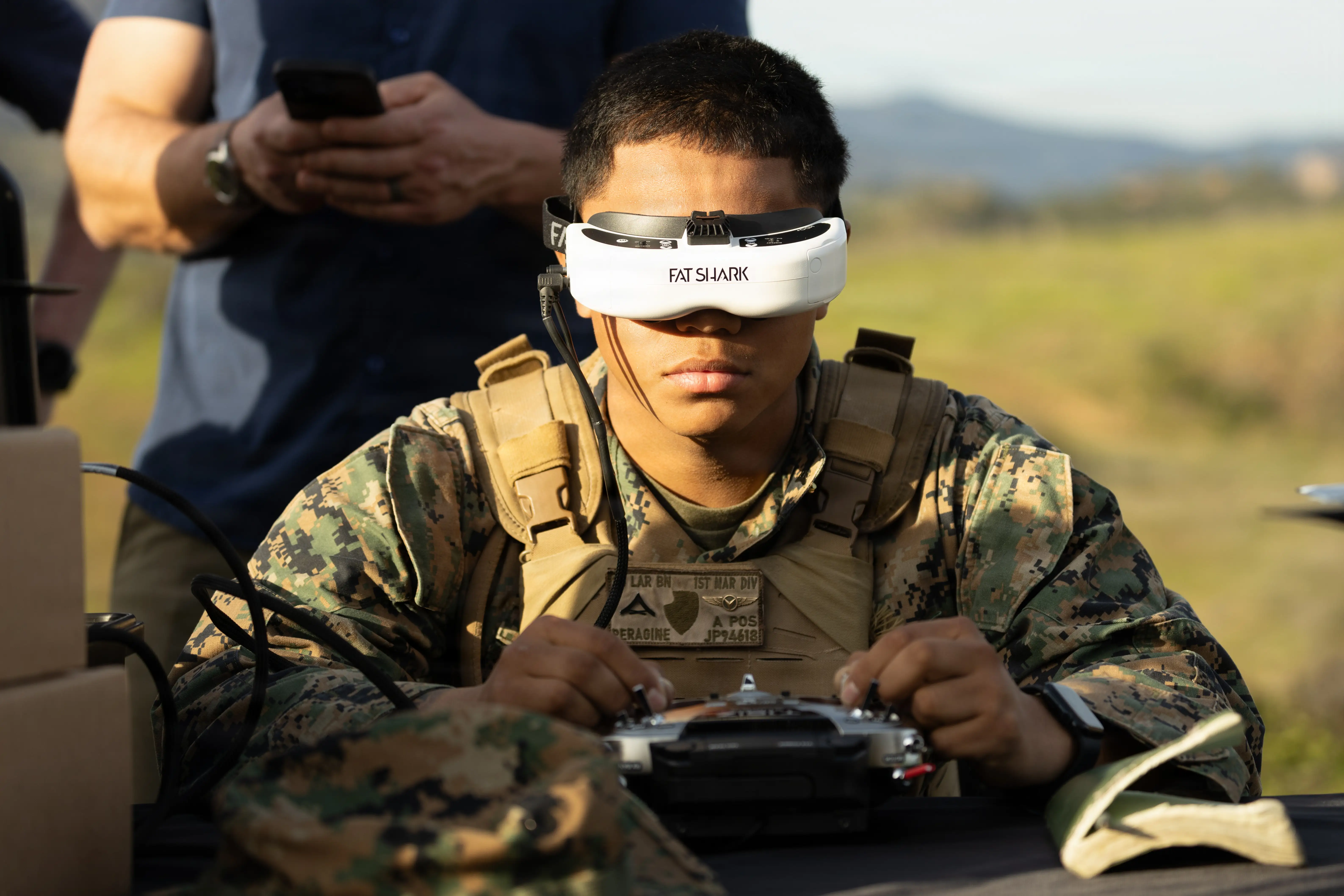 A man sits with a VR headset on and holds a drone controller.