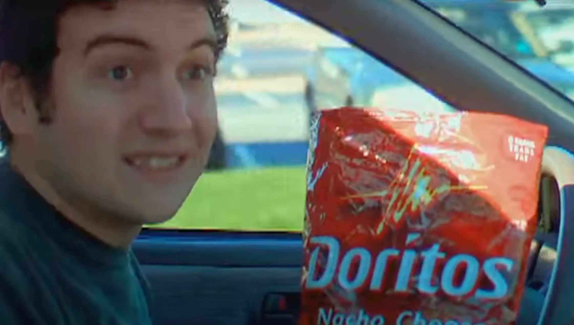 Man smiling as he drives while holding a bag of Doritos.