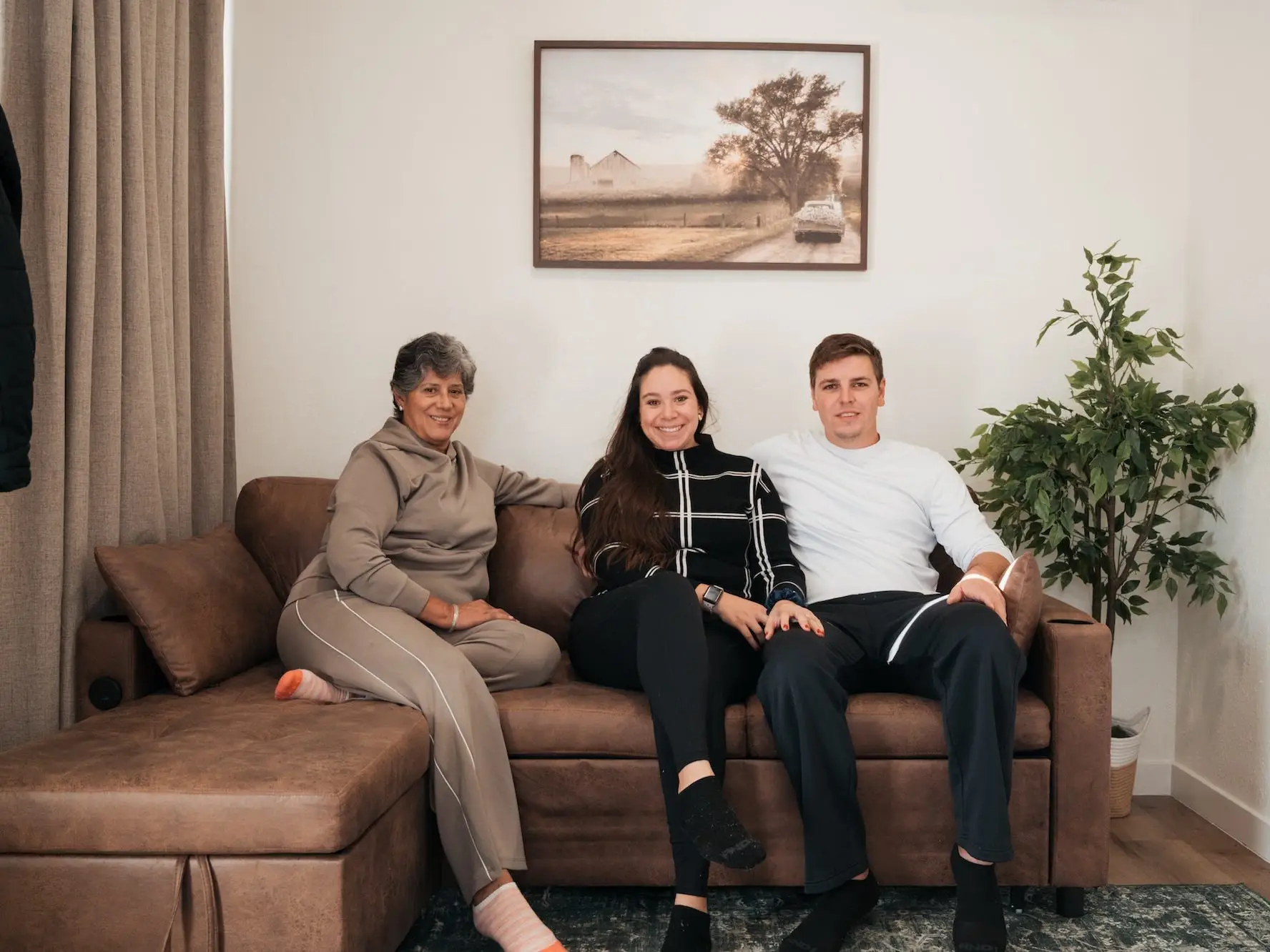 A mother sits on a couch with her daughter and son in-law.