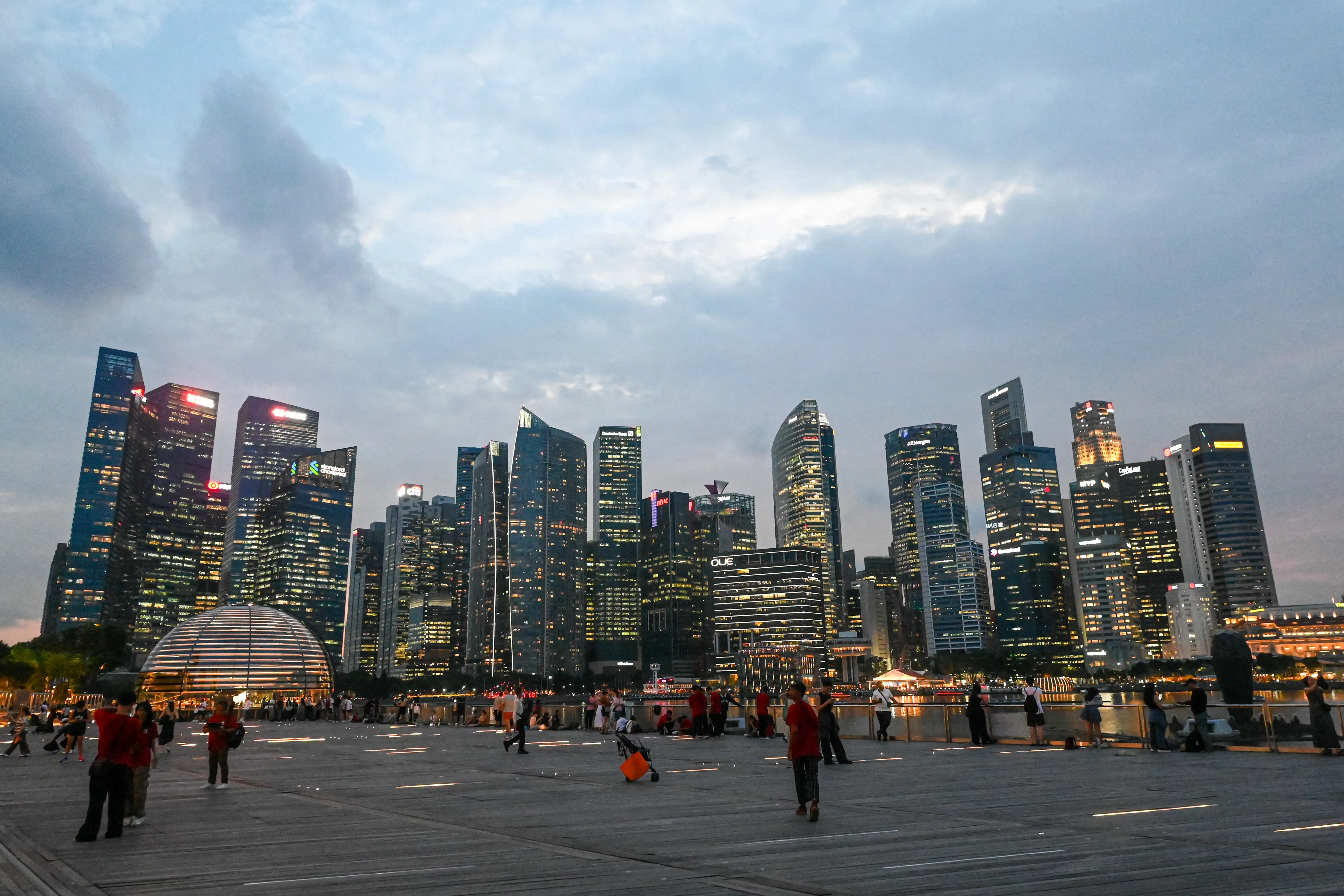 People gather along the boardwalk in front of the skyline at Marina Bay in Singapore