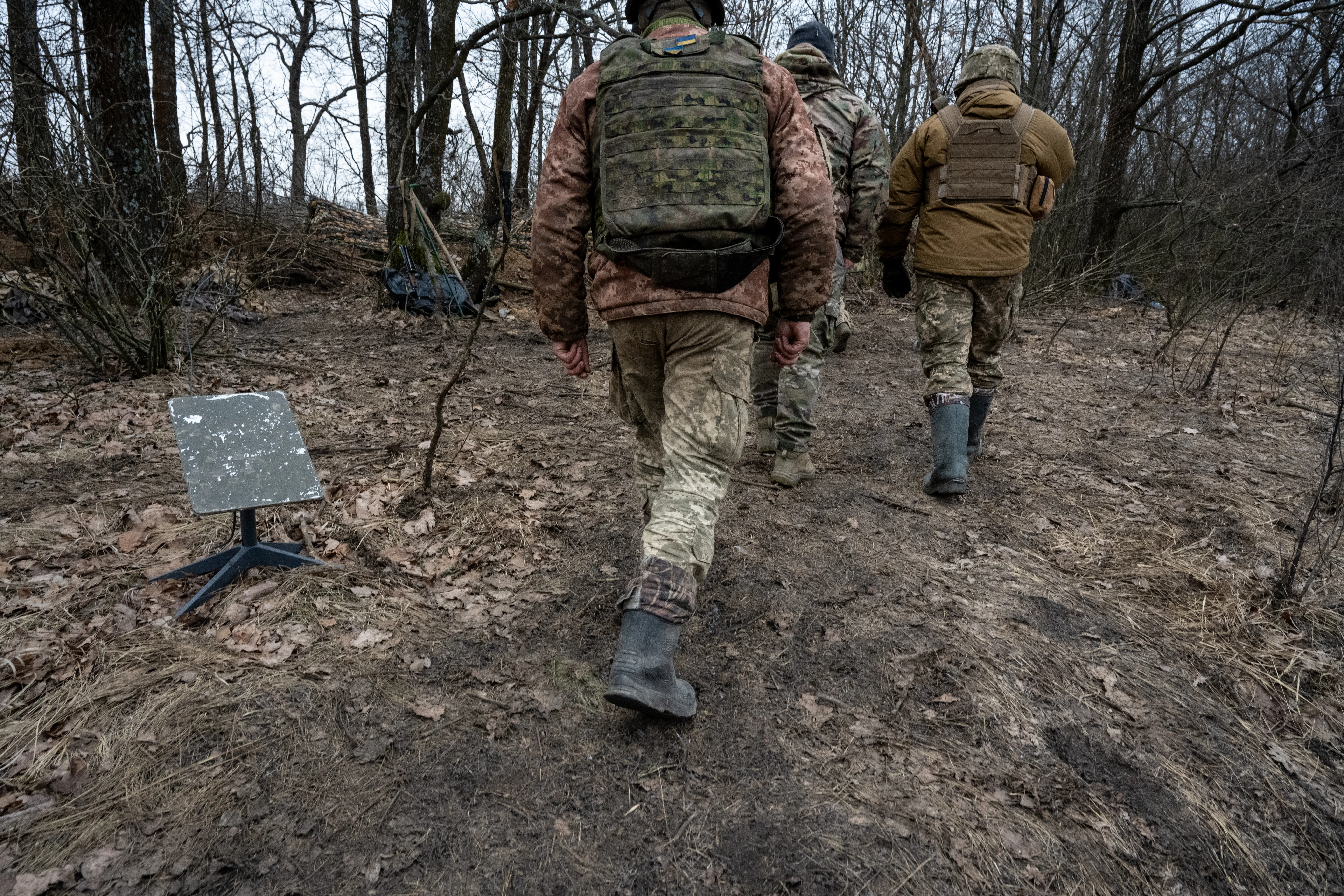 Ukrainian troops walk past a Starlink terminal in the forest.