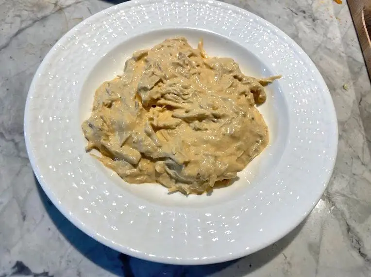 Buffalo-chicken dip on a white plate. The dip has visible shreds of chicken mixed in.