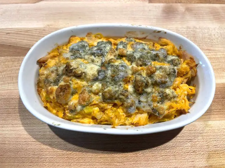 A casserole dish filled with yellow Buffalo-chicken dip with a pieces of golden-brown, bubbly blue cheese on top.