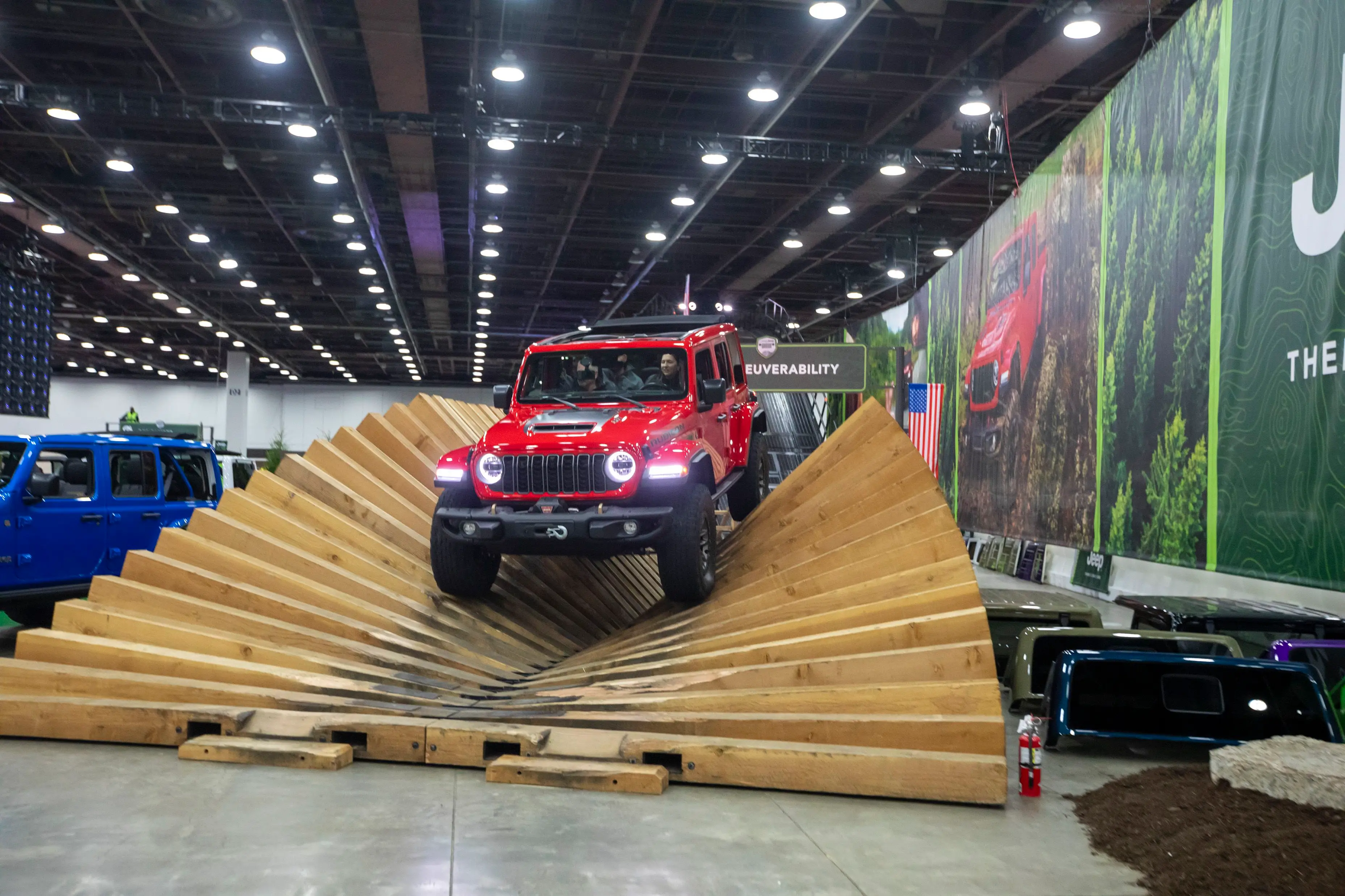 A red Jeep Wrangler SUV drives over a wooden maneuverability course during the Detroit Auto Show.