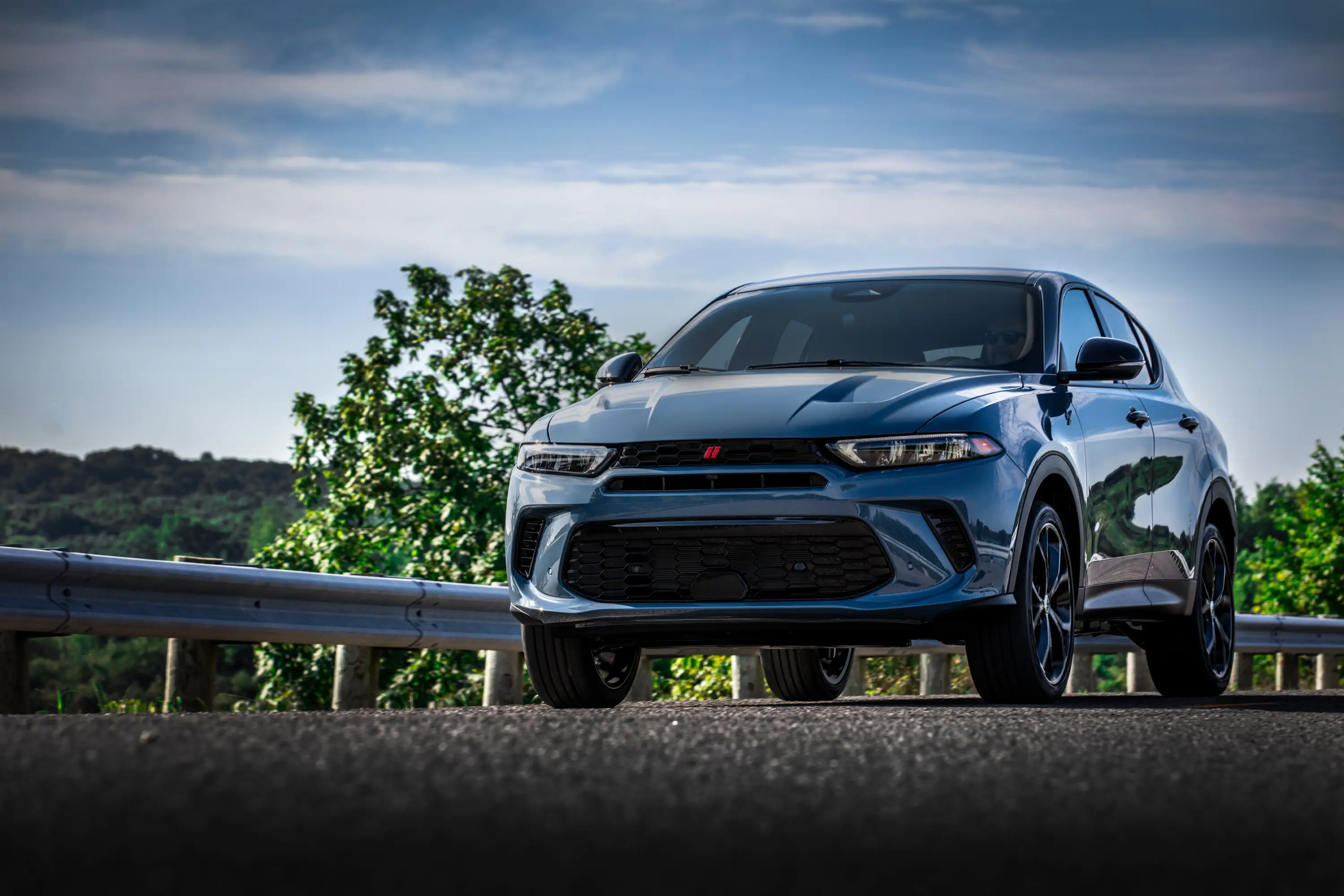 A light blue Dodge Hornet is parked on a street next to a guard rail.
