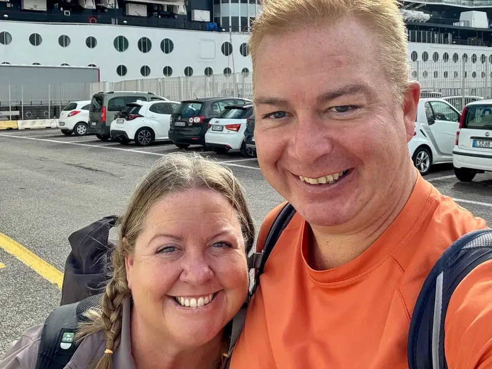 Author Tammy Barr and husband smiling in front of Celebrity cruise ship from parking lot