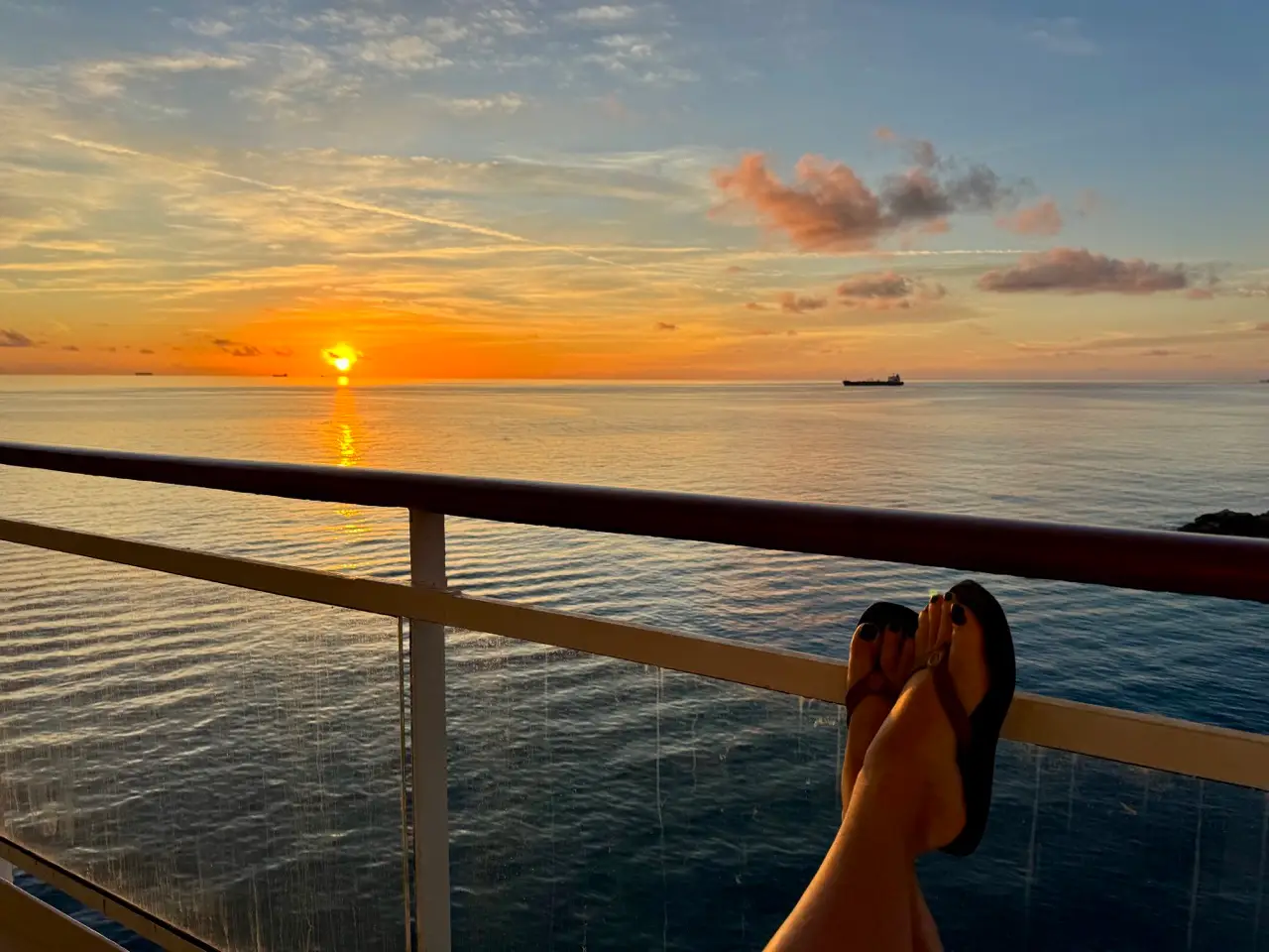 Woman's legs crossed in front of balcony on cruise ship at unset