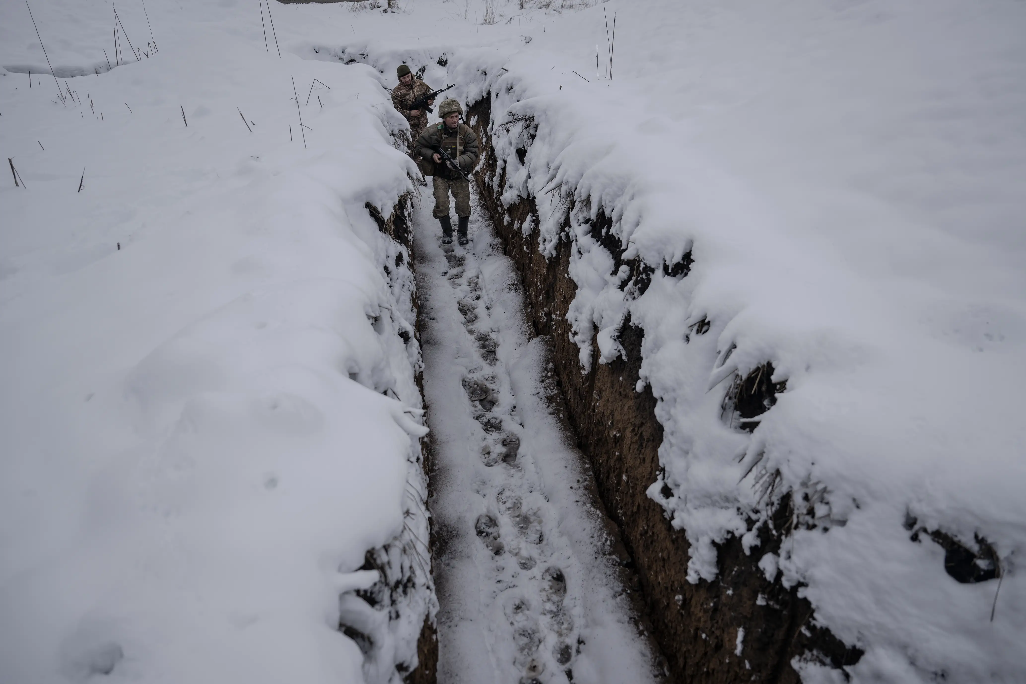 Two Ukrainian soldiers hold rifles as they walk along a trench line in Kharkiv.