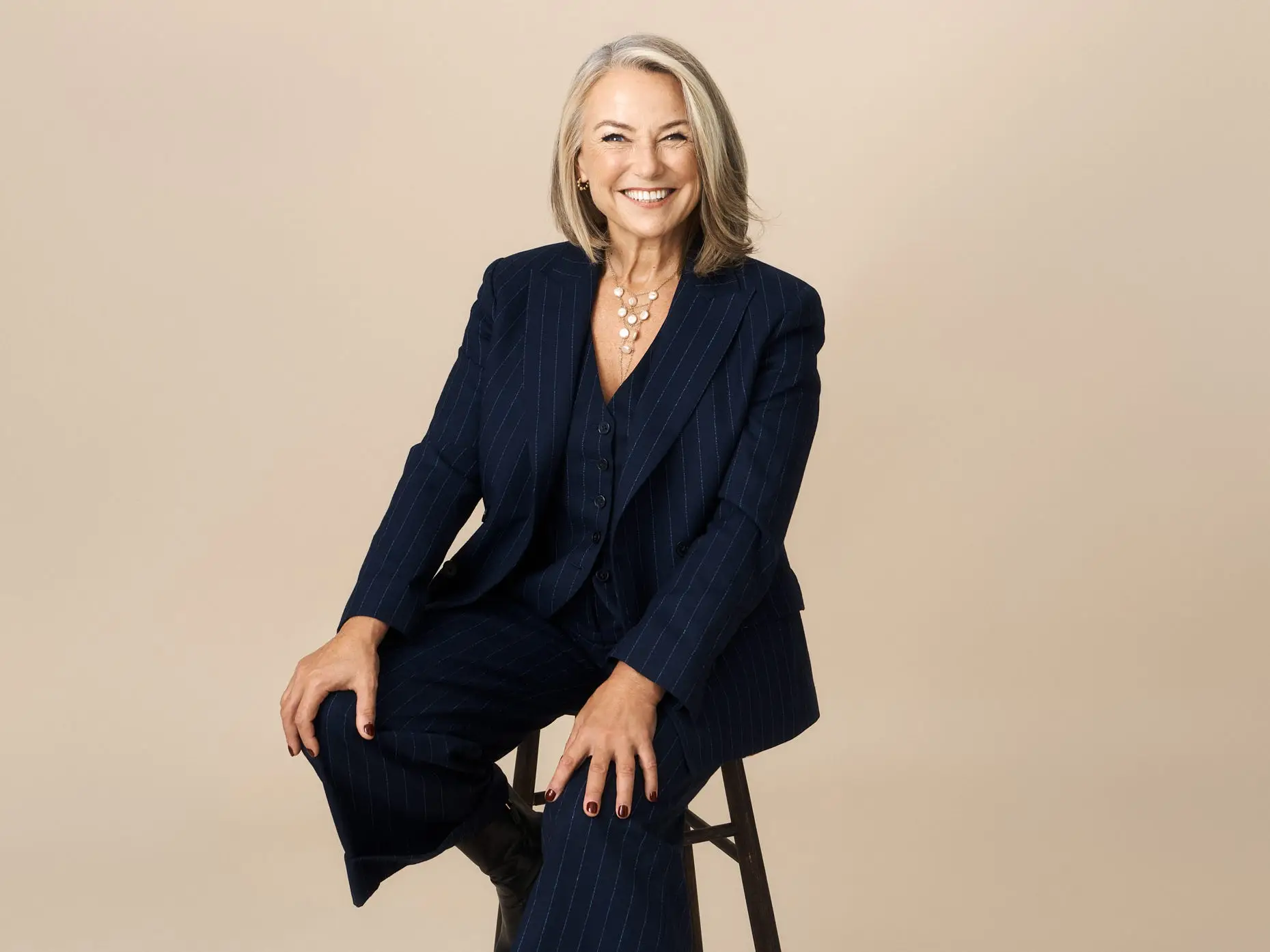 Esther Perel sitting on a black stool in front of a beige background