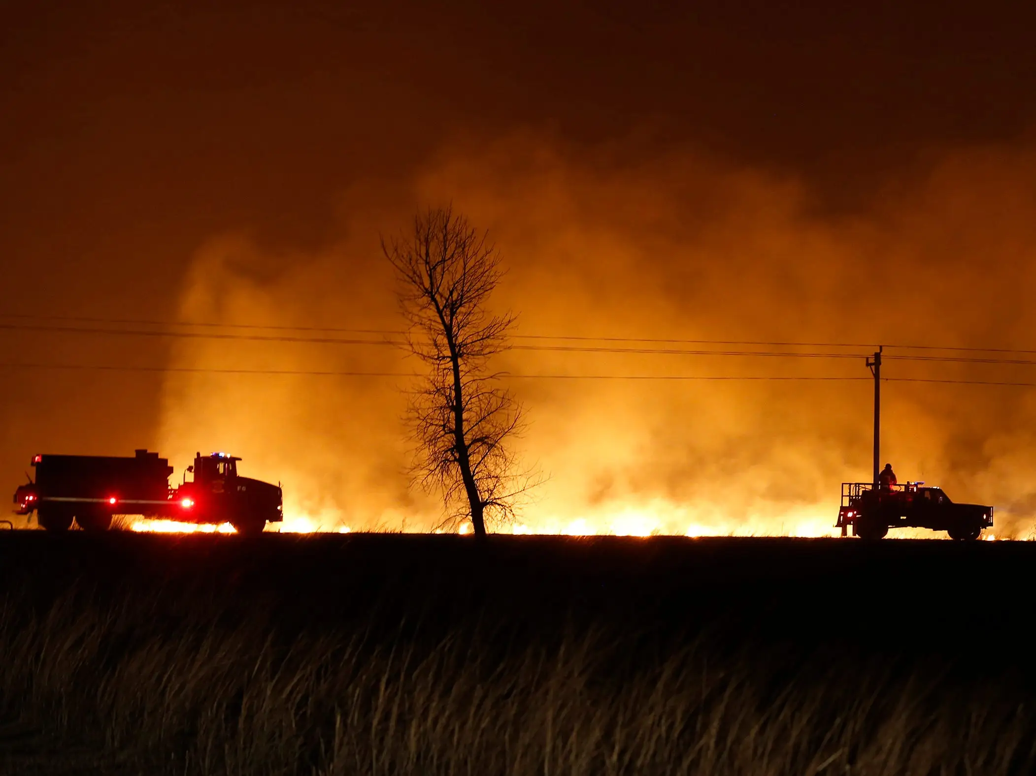 Emergency Medical Services vehicles in front of a backdrop engulfed with flames responding to a wildfire near protection, Kansas.
