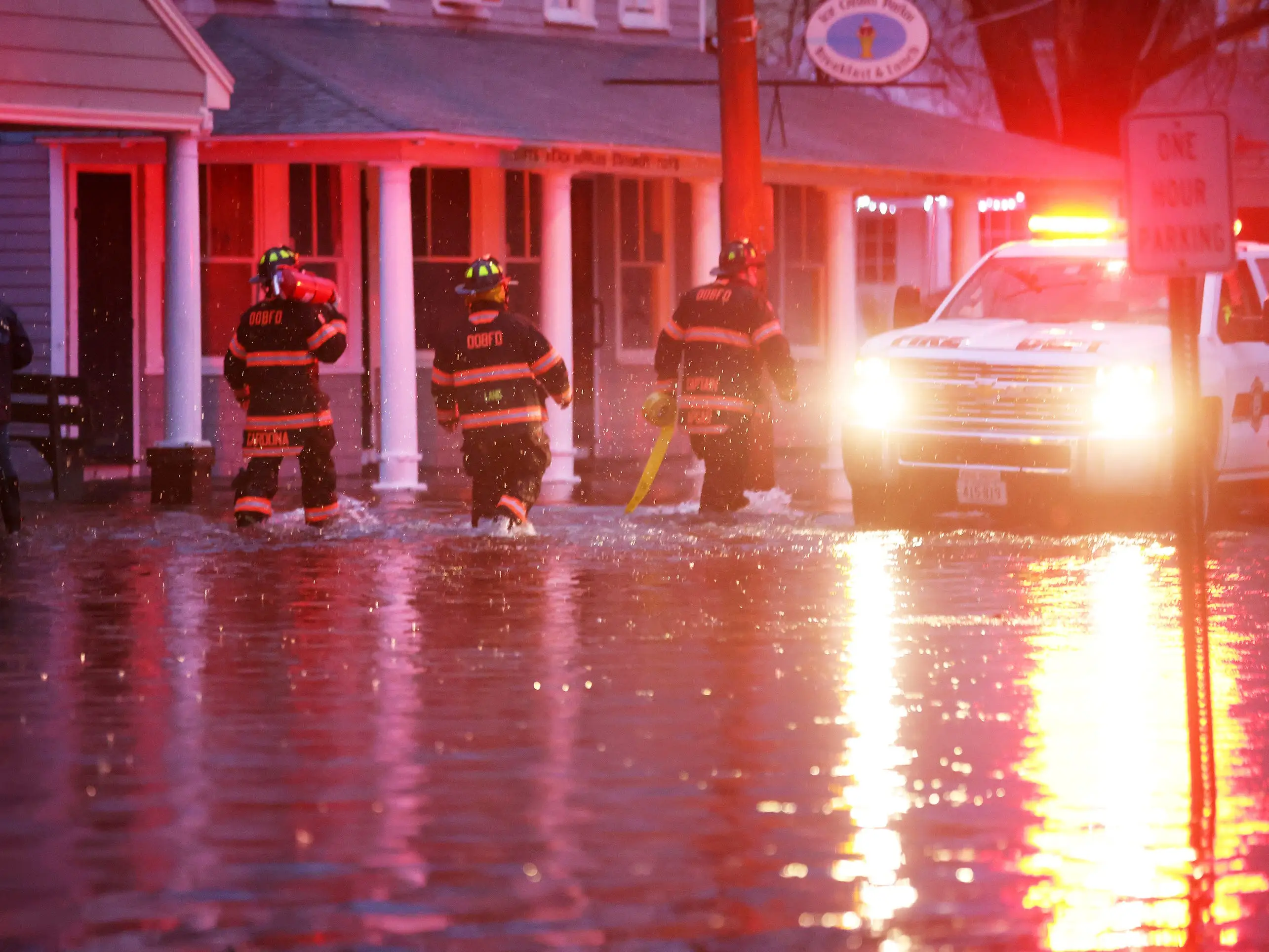Three firefighters walk through floodwaters during an emergency response in Ocean Park, Maine.
