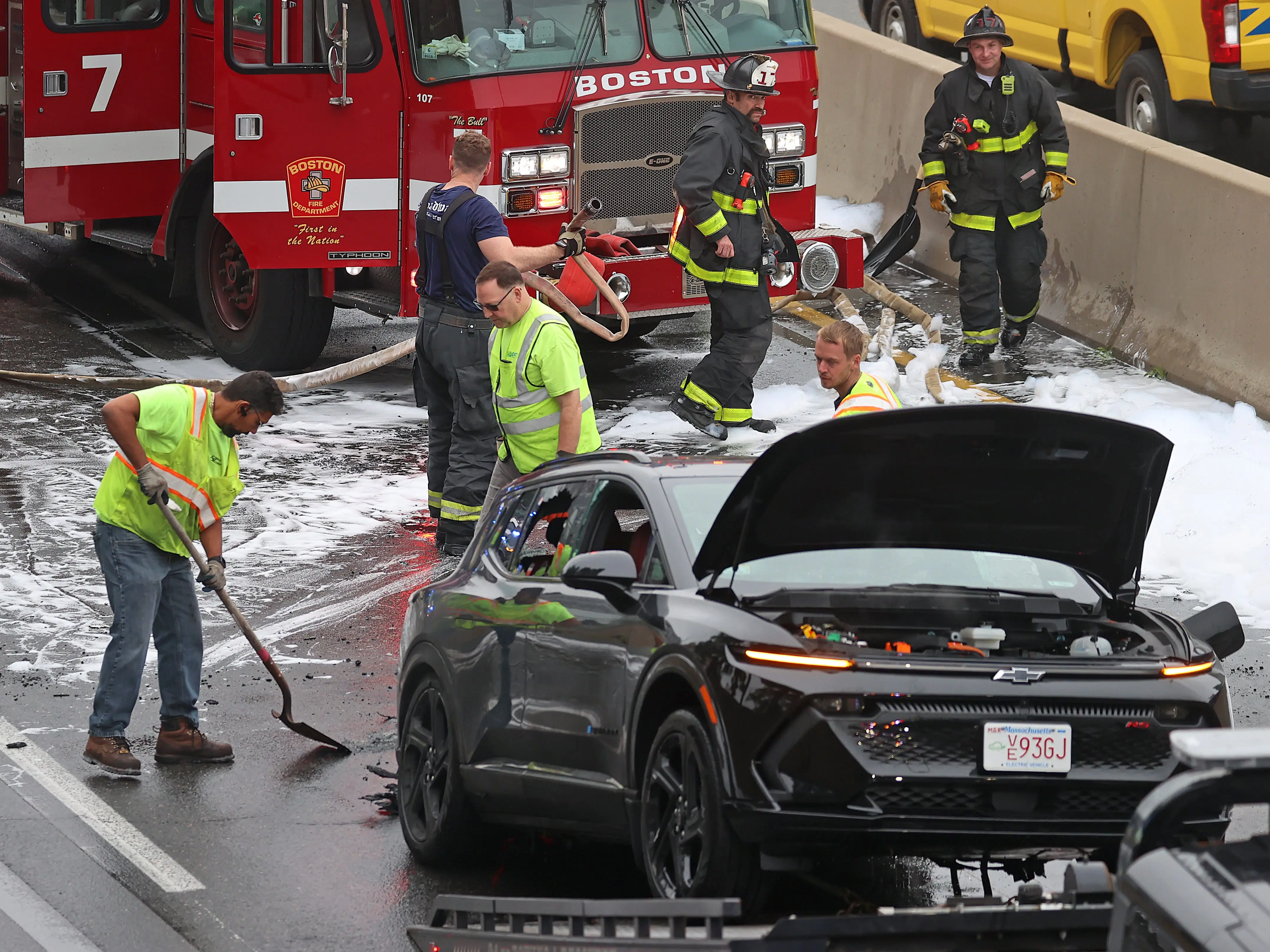 Firefighters cleaning up the roadway after extinguishing an electric car fire in Boston, MA.