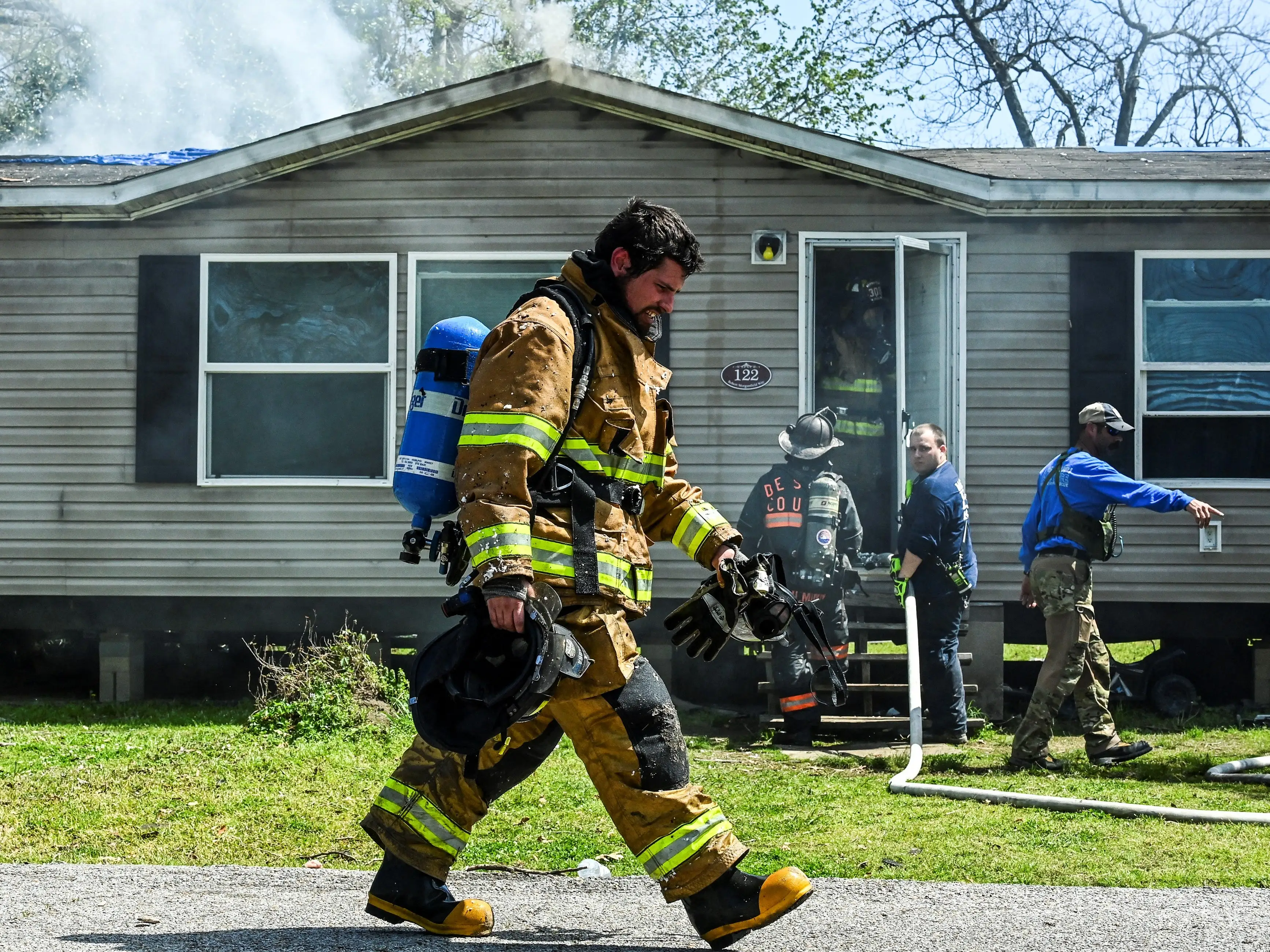 A firefighter dressed in full equipment walks past a damaged house in Rolling Fork, Mississippi.