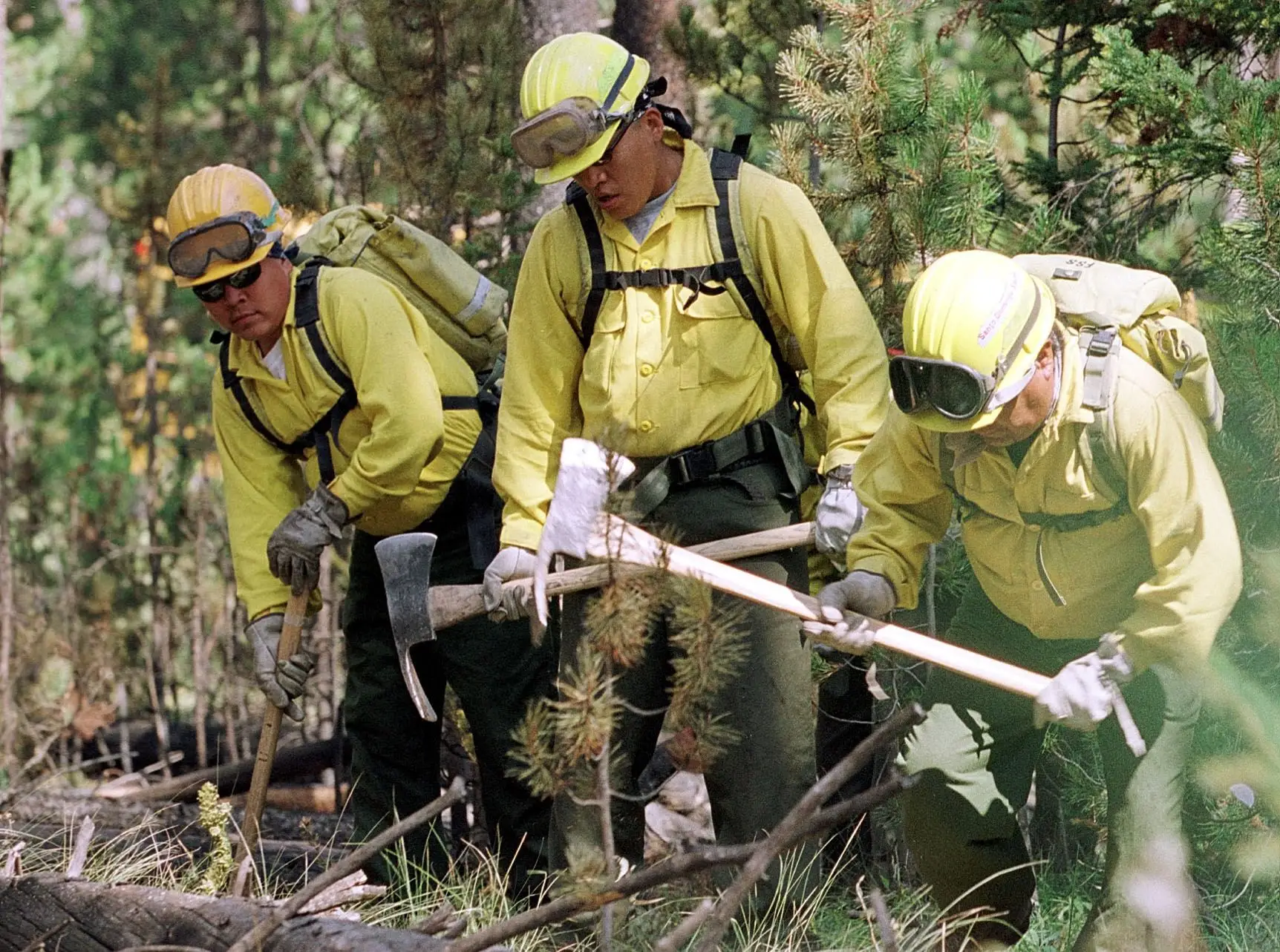 Three firefighters work with axes near Yellowstone National Park in Wyoming.