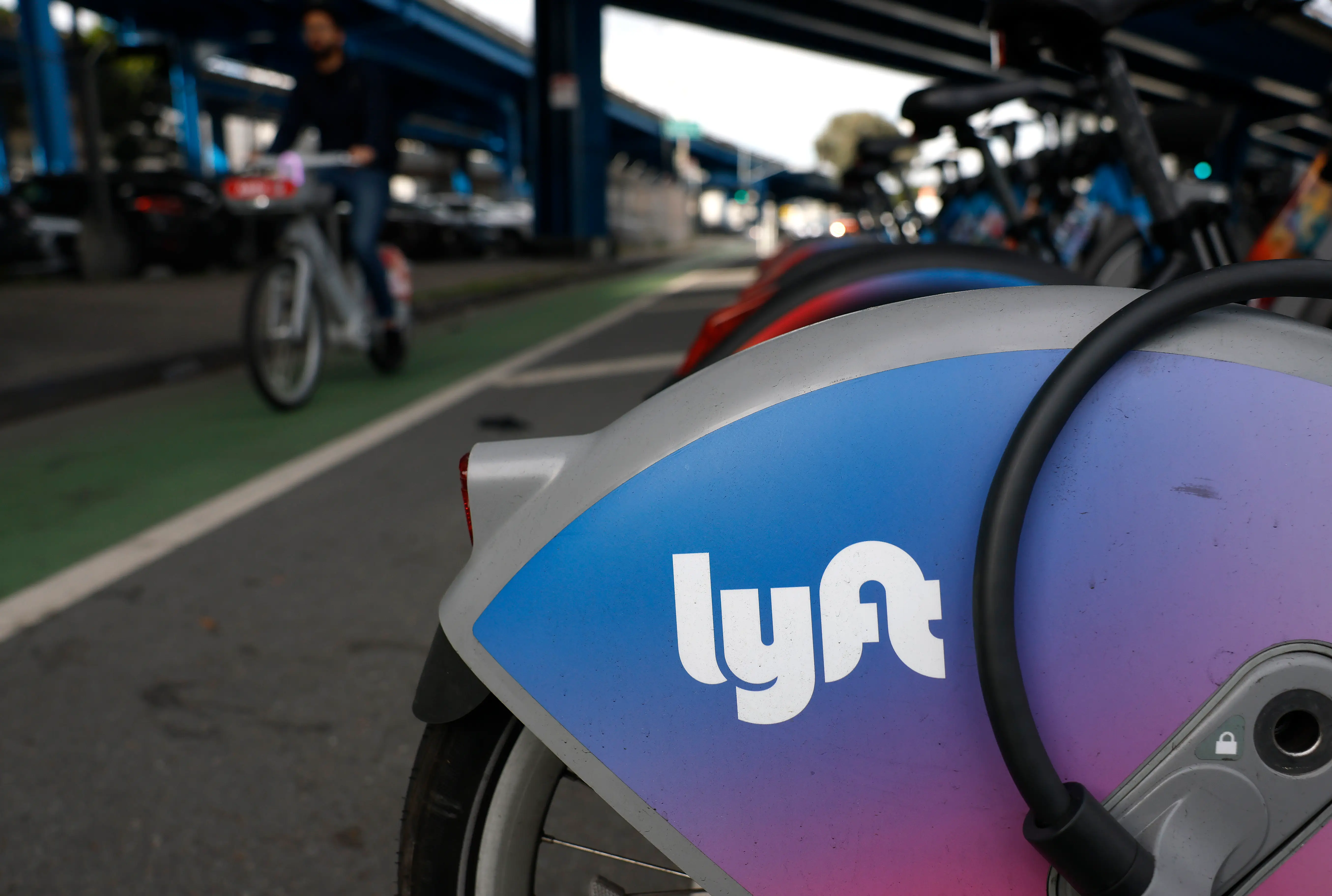 A Lyft rental bike is seen from its rear wheel as a user rides another bike in a bike lane in the background