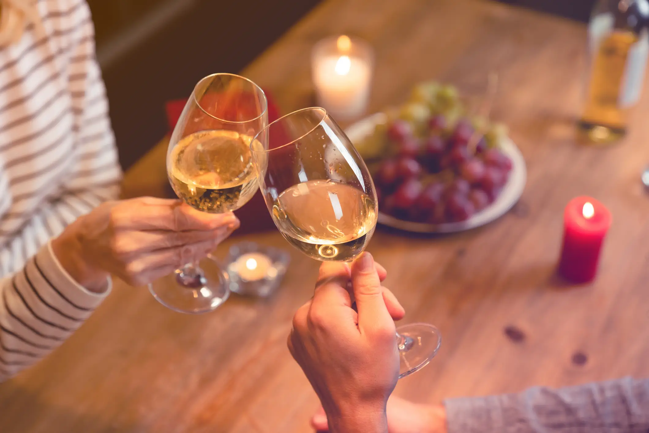 Two hands clinking glasses of wine over a romantic dinner.