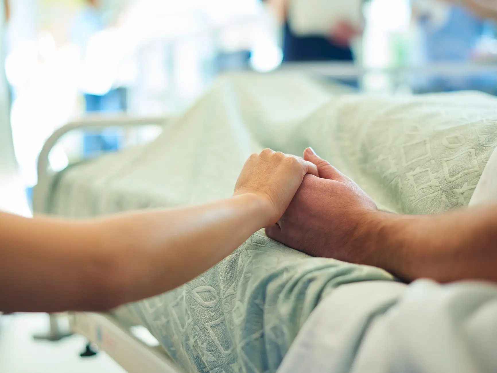 A visitor holding hands with a patient in a hospital bed.