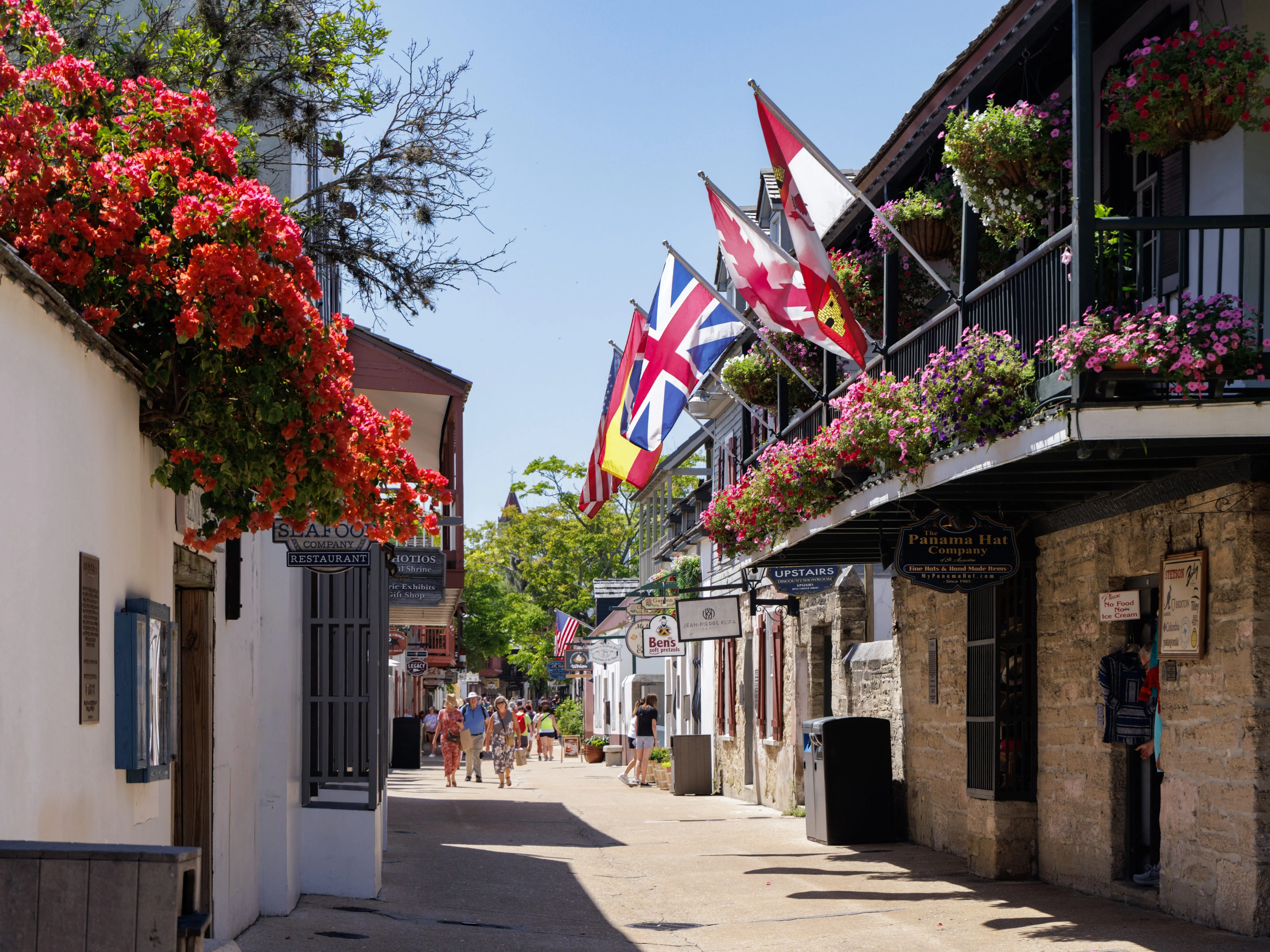 A busy St. George Street in St. Augustine, Florida, lined with historic buildings, flags, and flowers