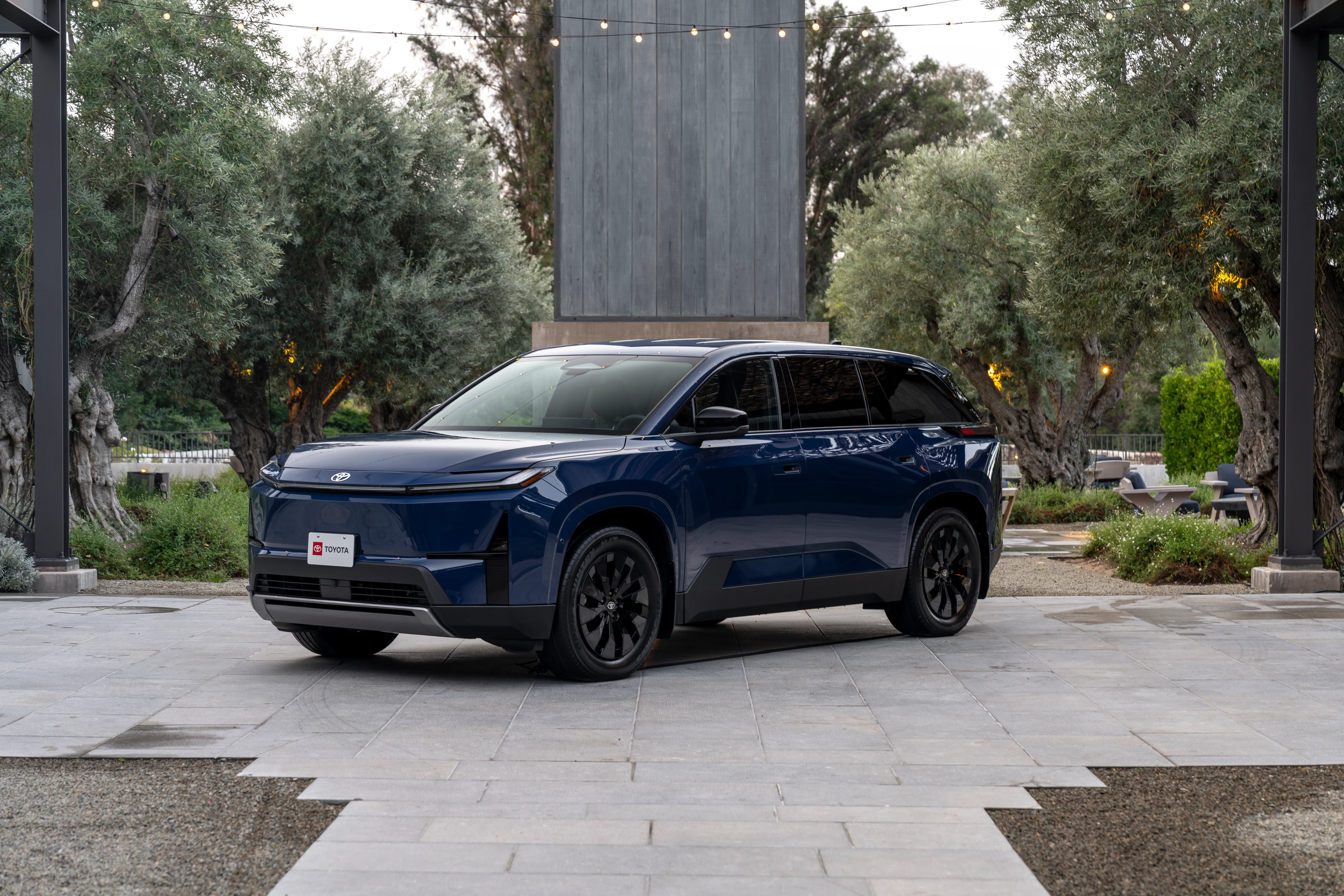 A dark blue 2027 Toyota Highlander EV is parked on a paver driveway. It has black rims and a light bar for its headlamps.