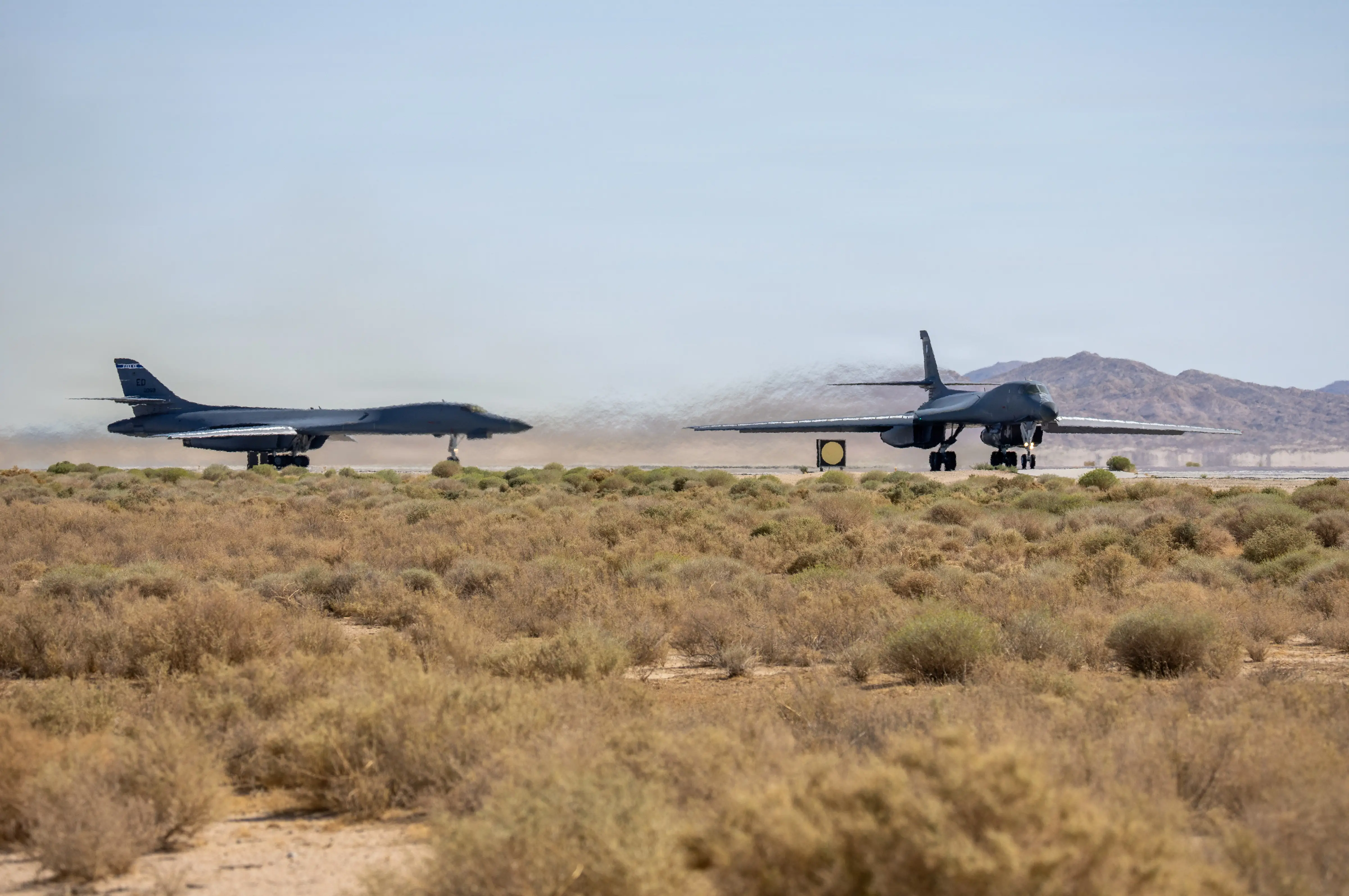 Two B-1 Lancer bombers sit on tarmacs in desert grasslands.
