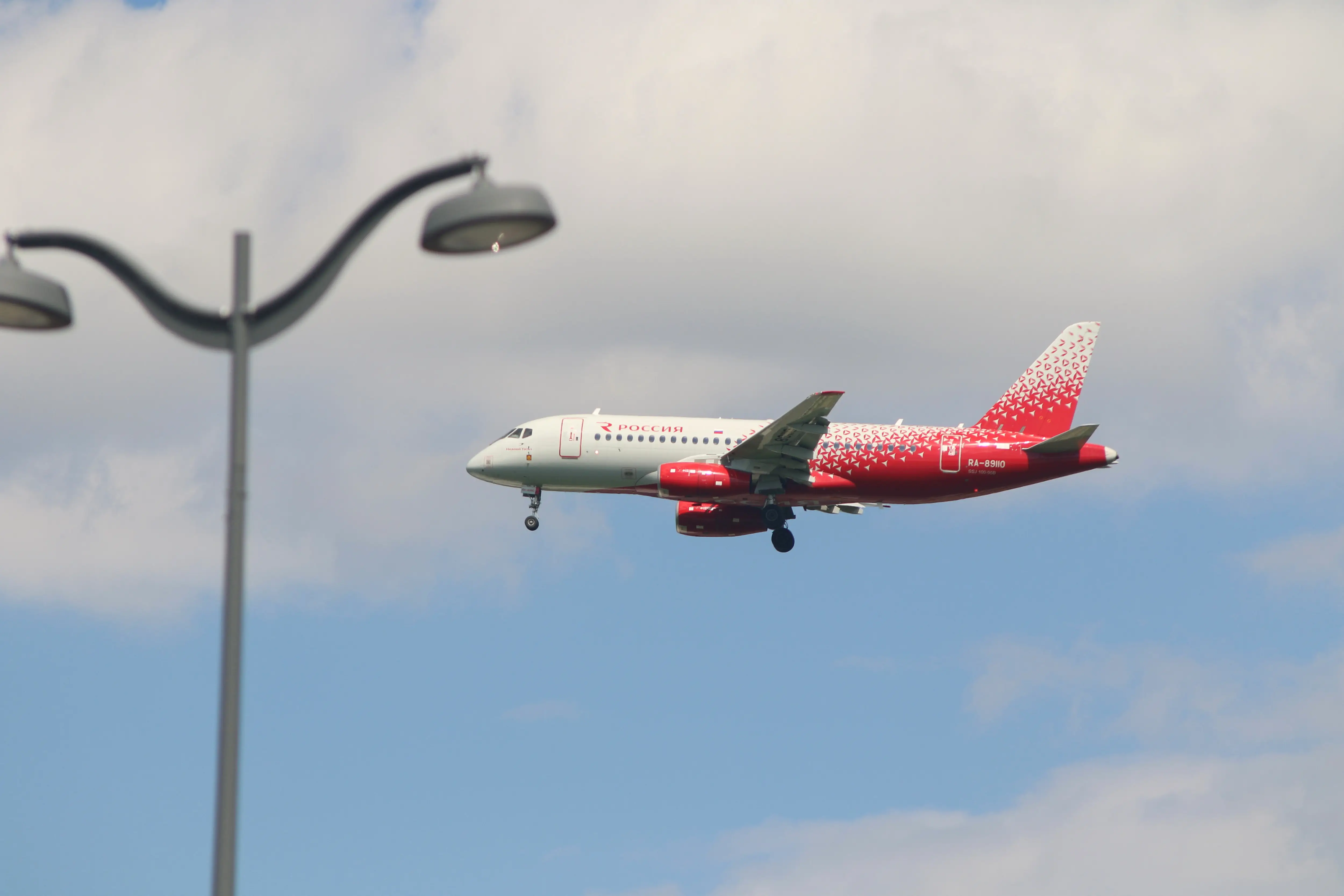 A Rossiya Sukhoi Superjet 100 aircraft flies above a lamp post.