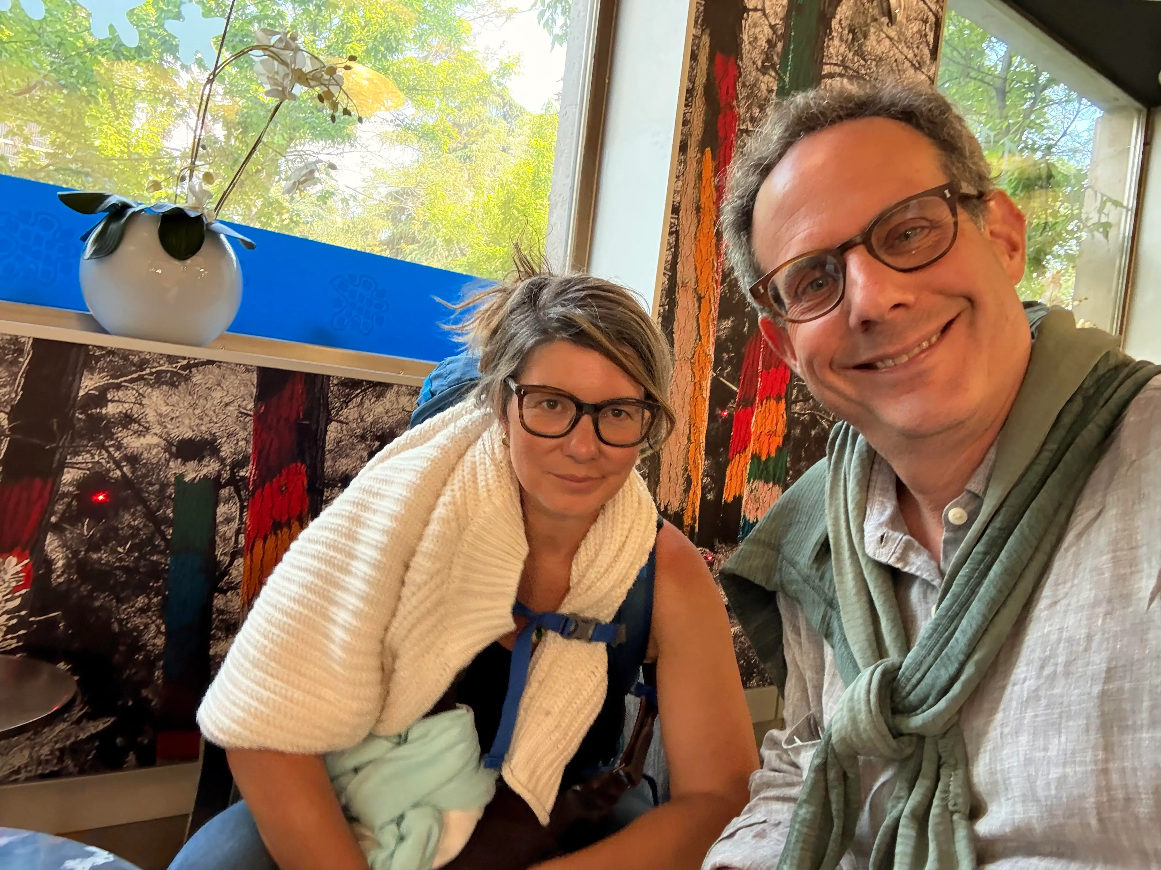 Man and woman in glasses with sweaters around their shoulders.