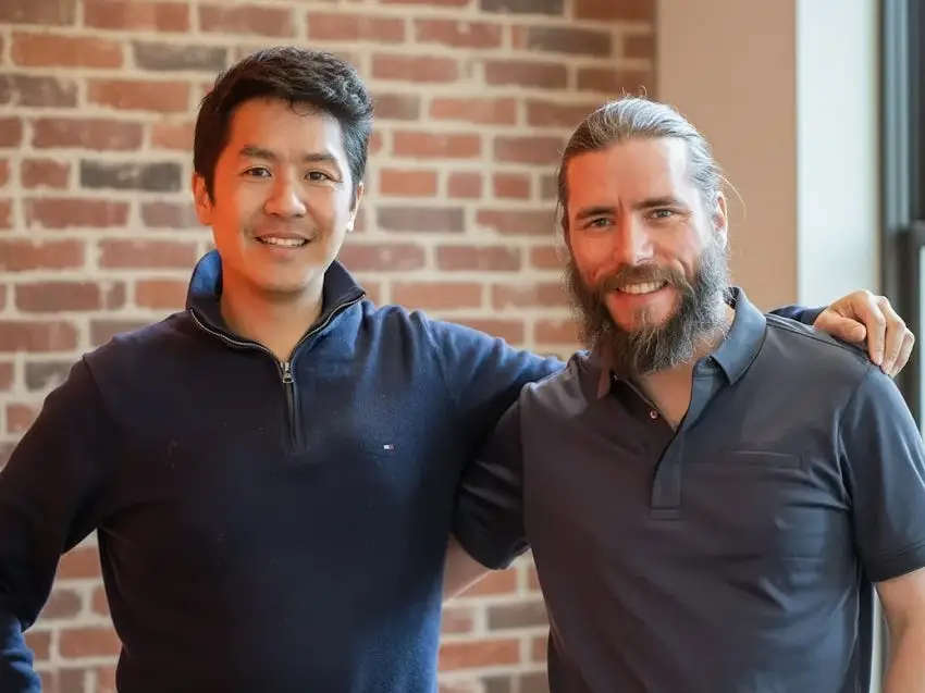 Vybe cofounders Quang Hoang and Fabien Devos with their arms around one another, standing in front of a brick wall.