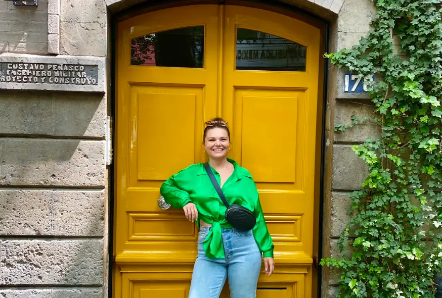 The writer posing in front of a colorful yellow door in Mexico City.