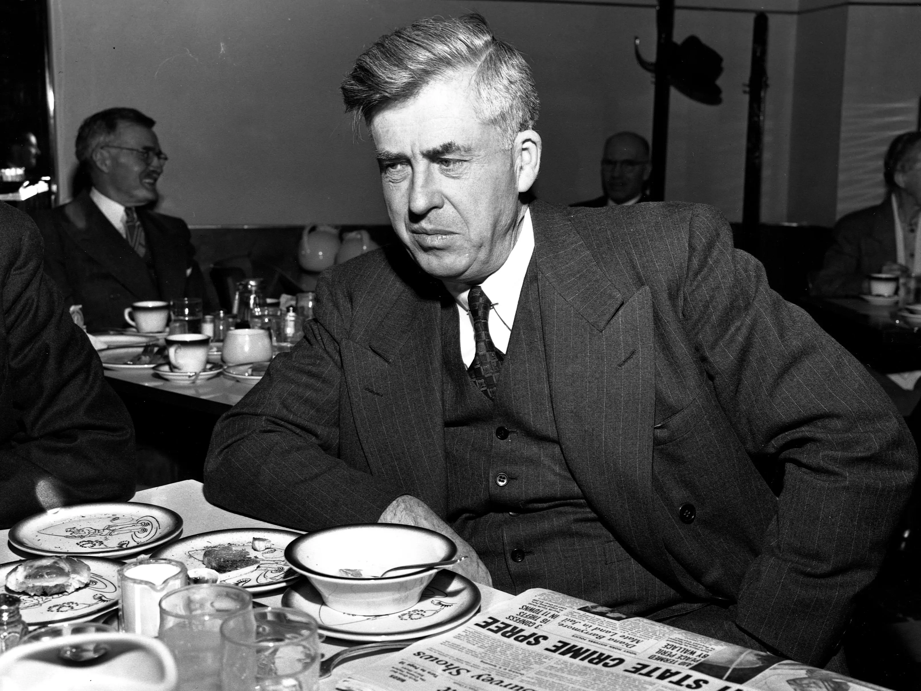 Henry Wallace reading a newspaper while eating breakfast.
