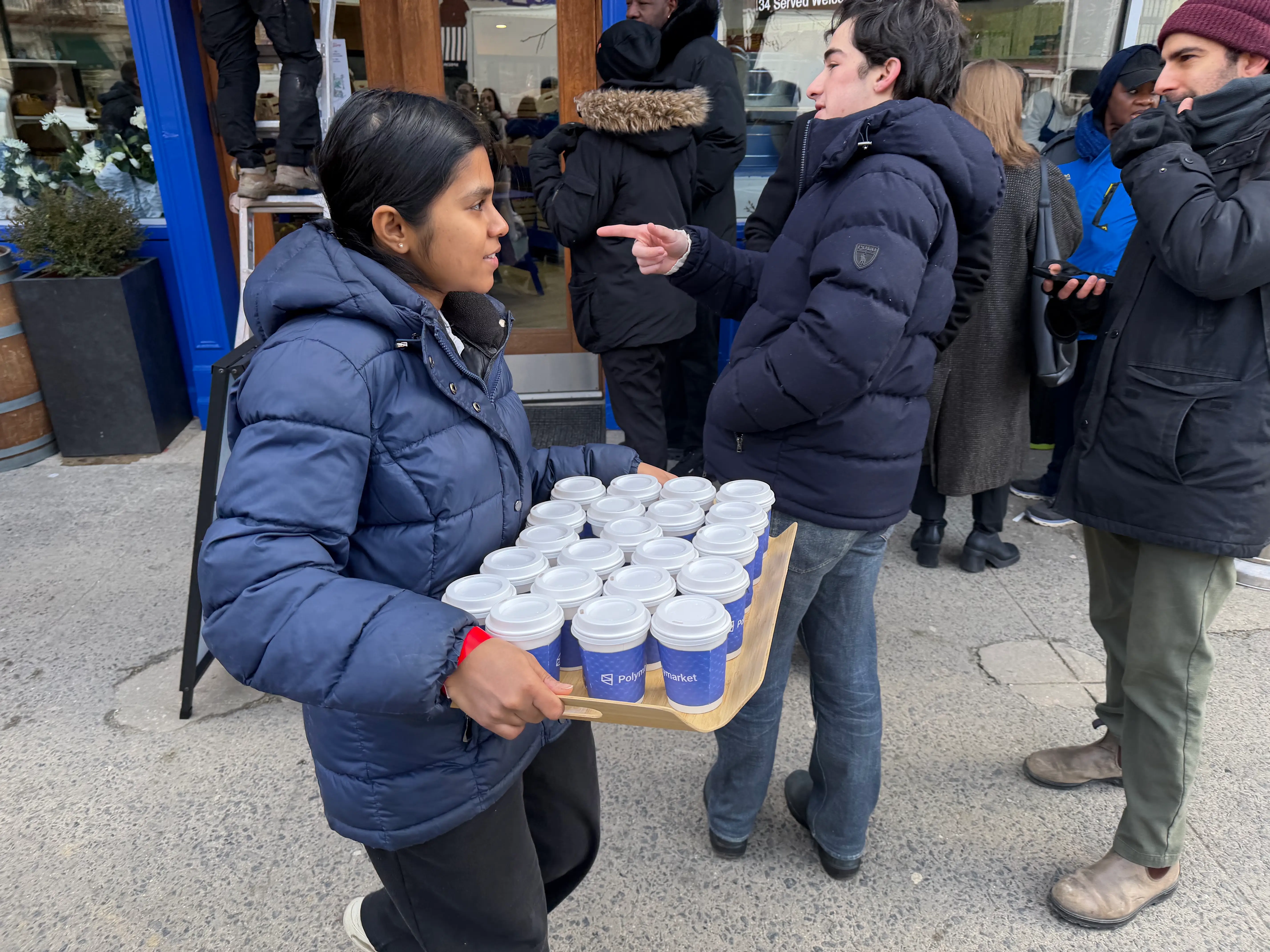 A staffer hands out cups of hot chocolate to those waiting in line for the Polymarket.