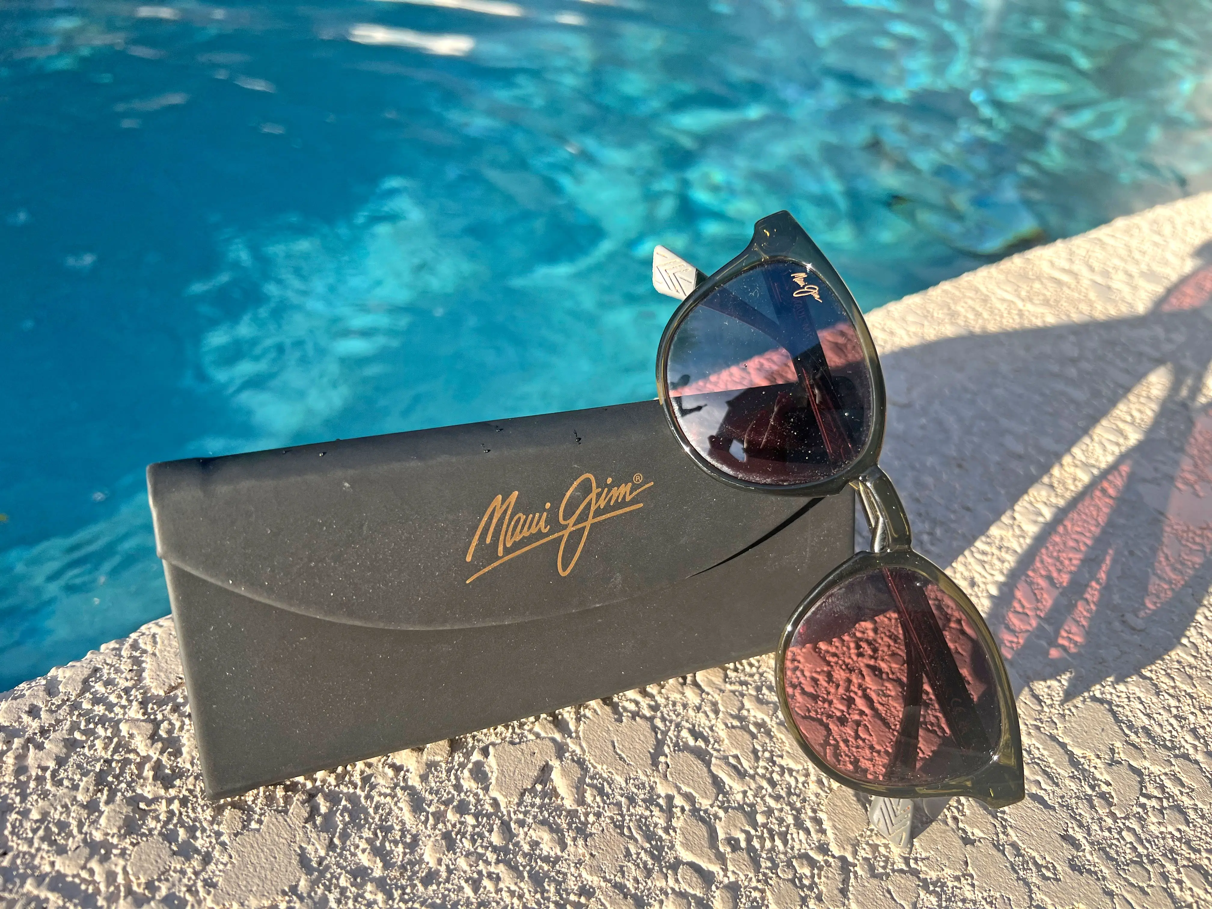 A pair of sunglasses and a case near a pool.