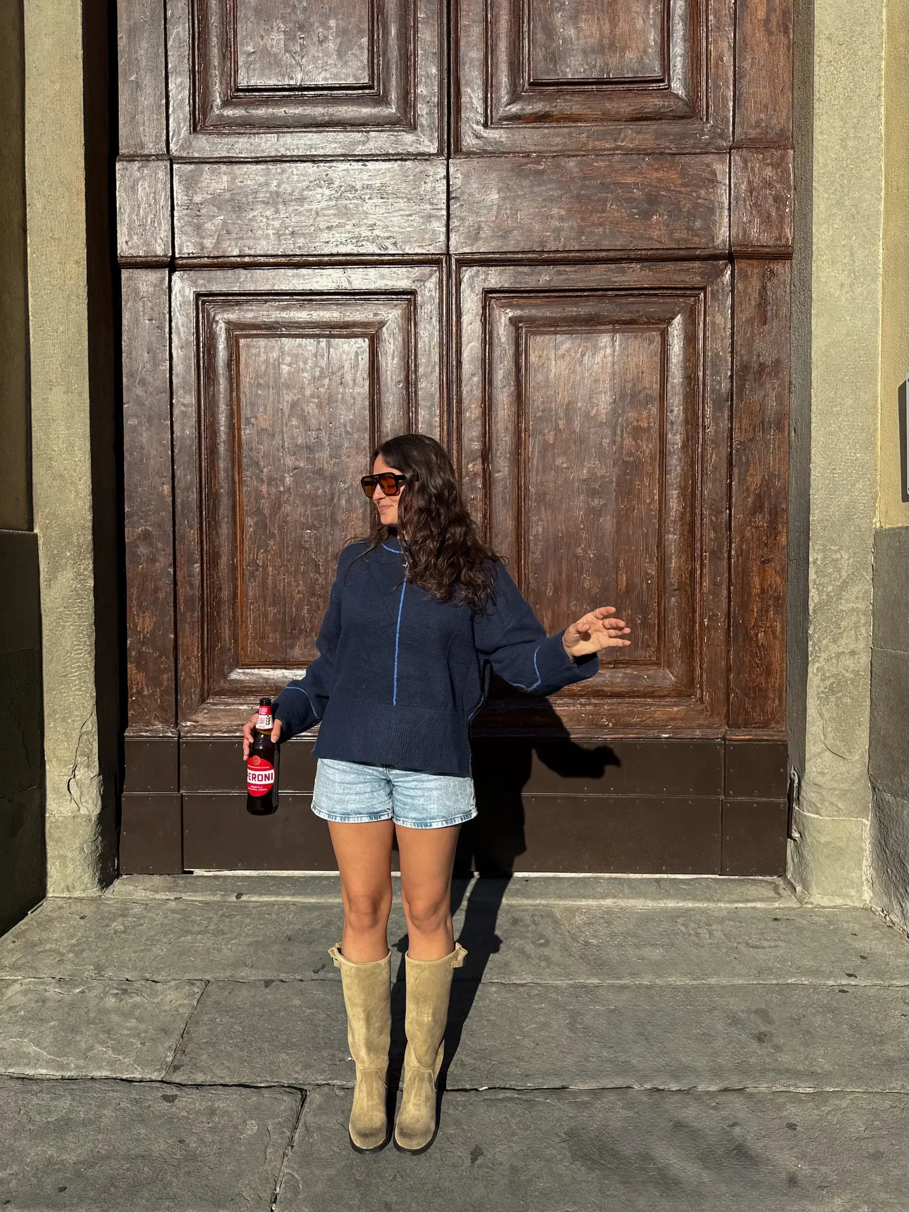 A woman posing holding a beer in front of a large door.