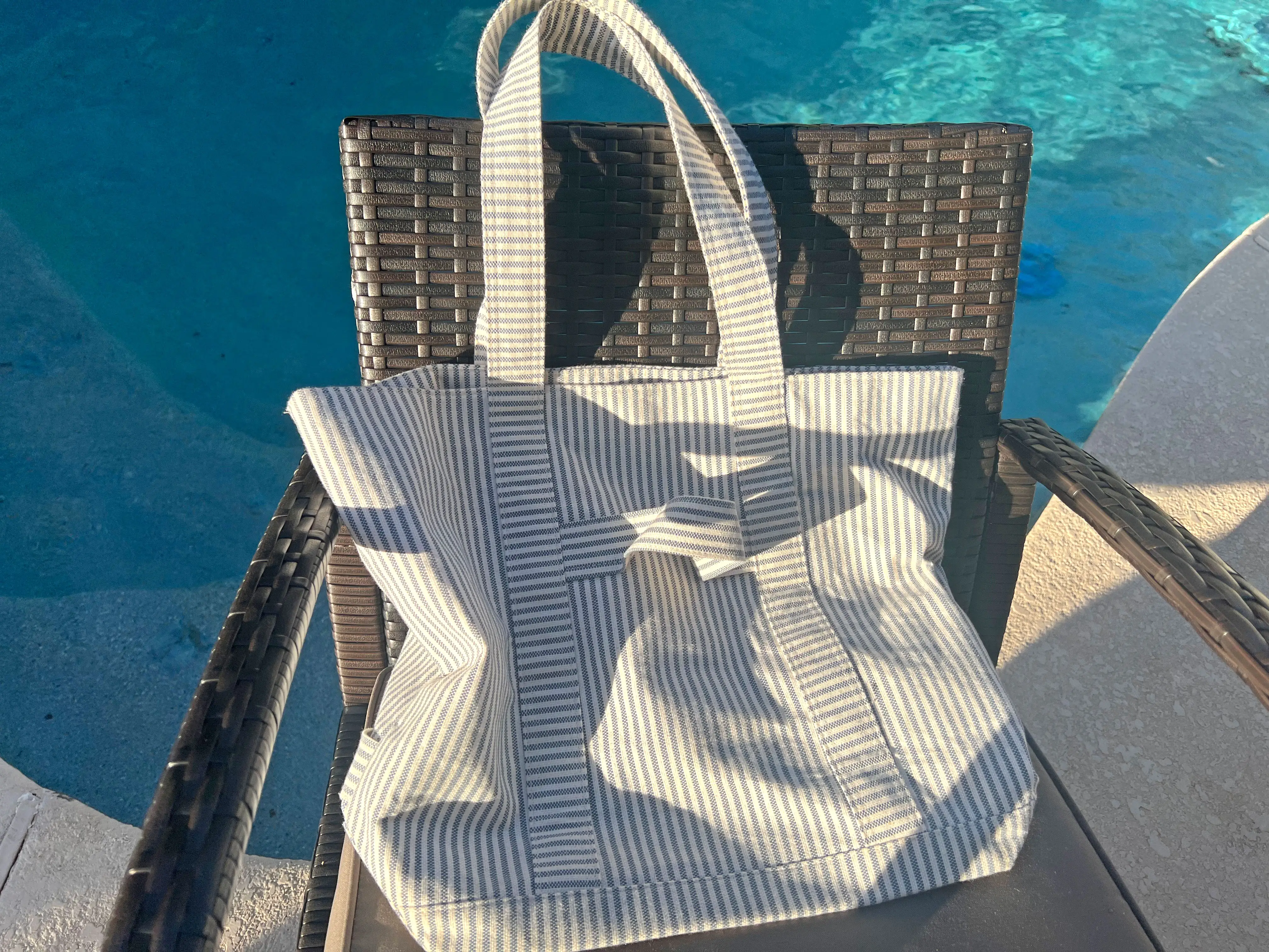 A small striped beach bag on a chair near a pool.