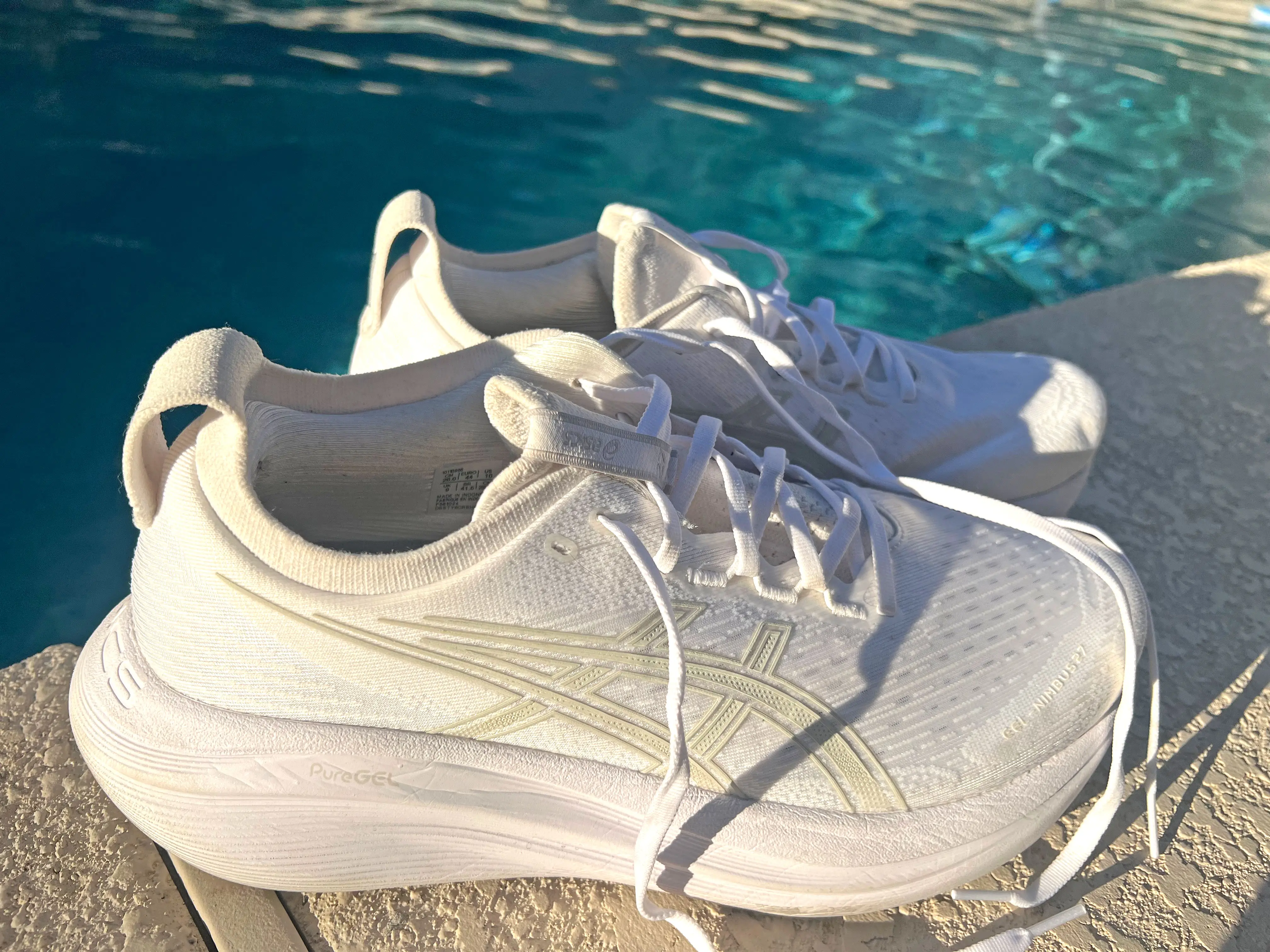 A pair of white sneakers next to a pool.