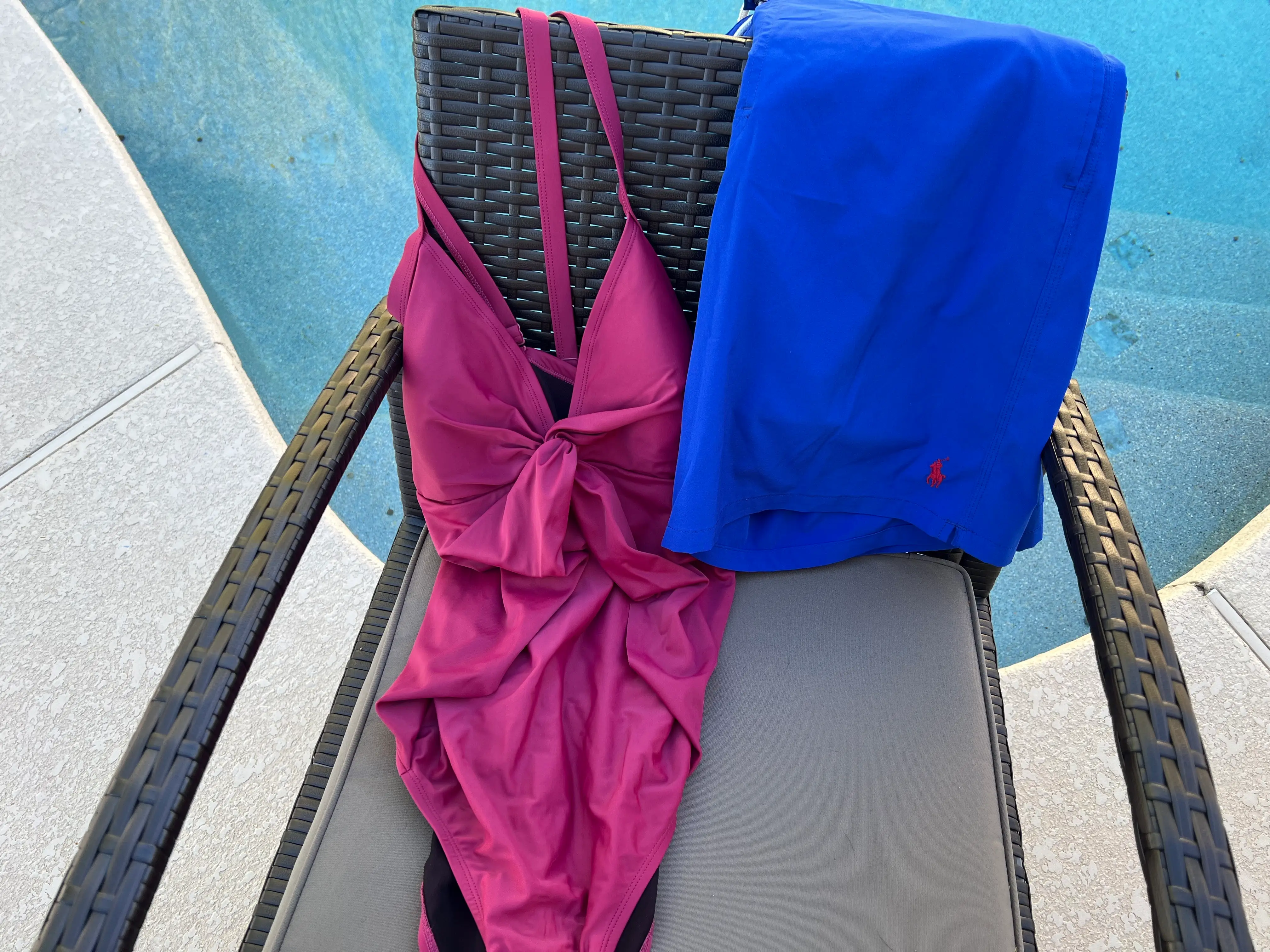 A pink bathing suit and a blue towel on a chair near a pool.