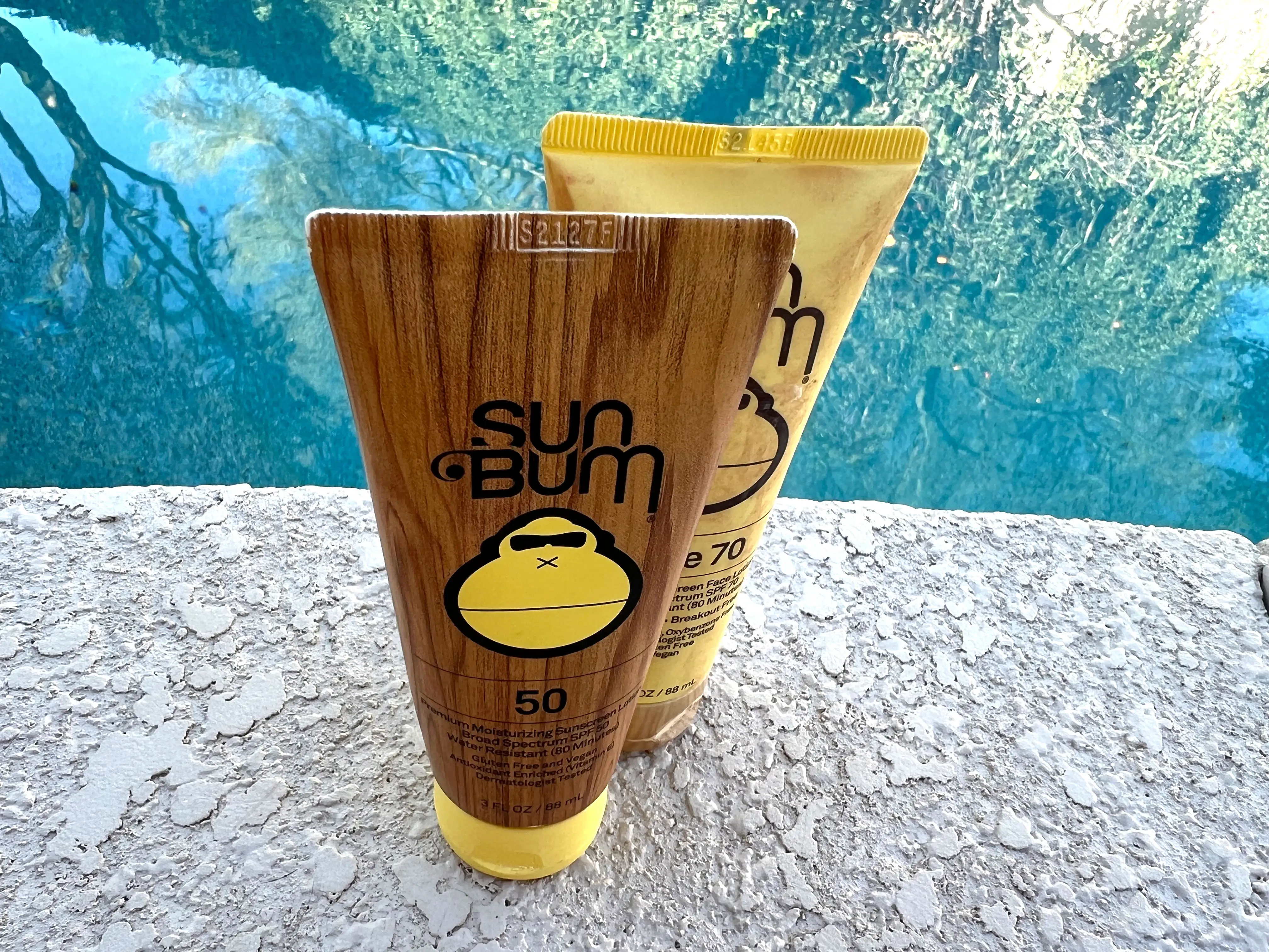 Two bottles of sunscreen near a pool.
