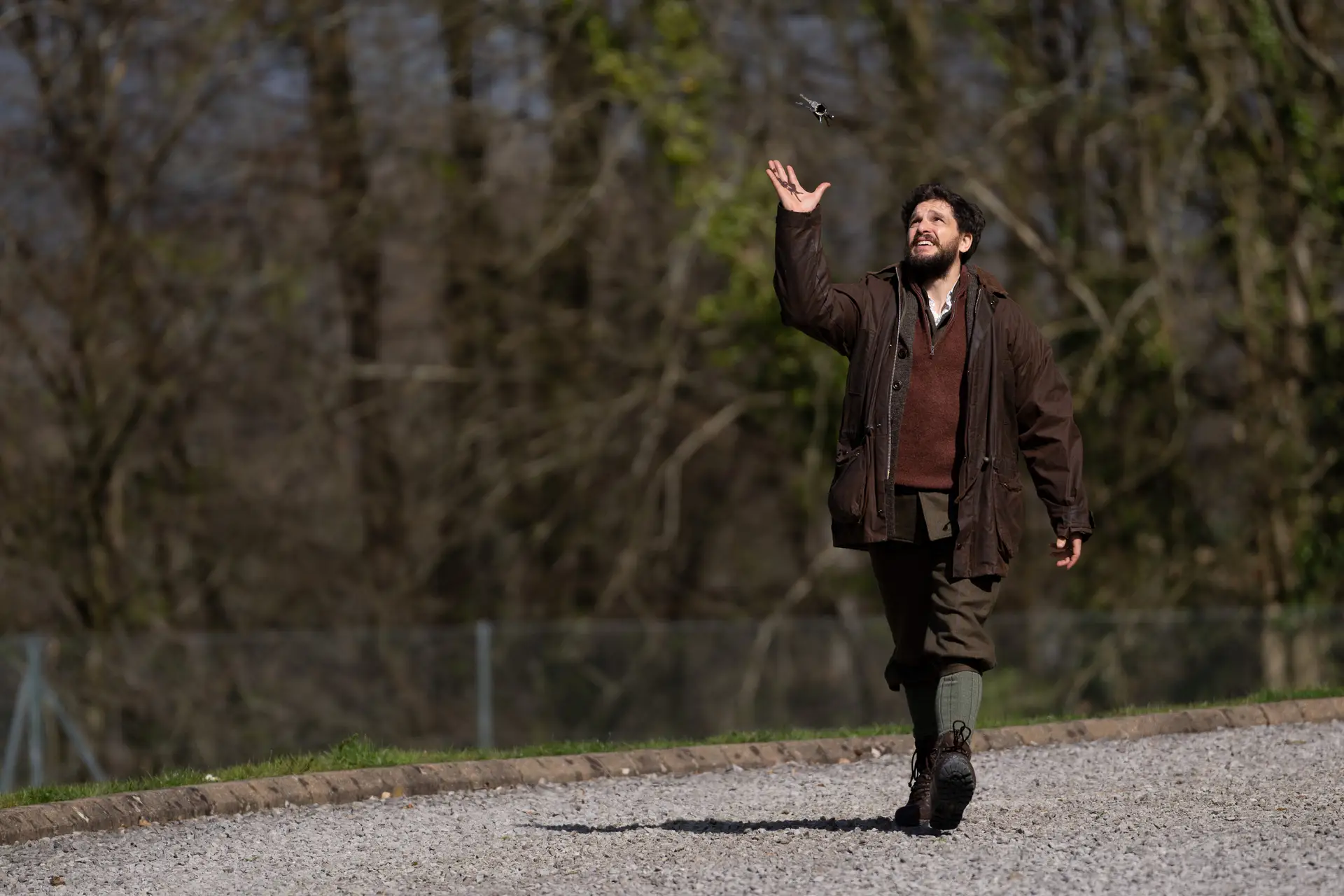 A man wearing a heavy coat on a path in the woods tosses his keys in the air