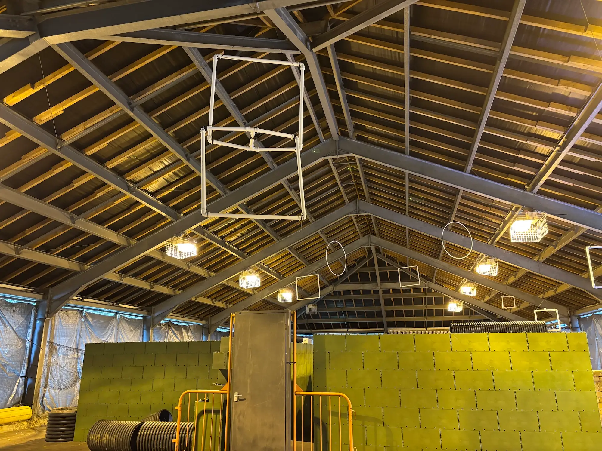 The inside of a structure with wooden and metal roof with white circle and square shaped objects hanging from the ceiling
