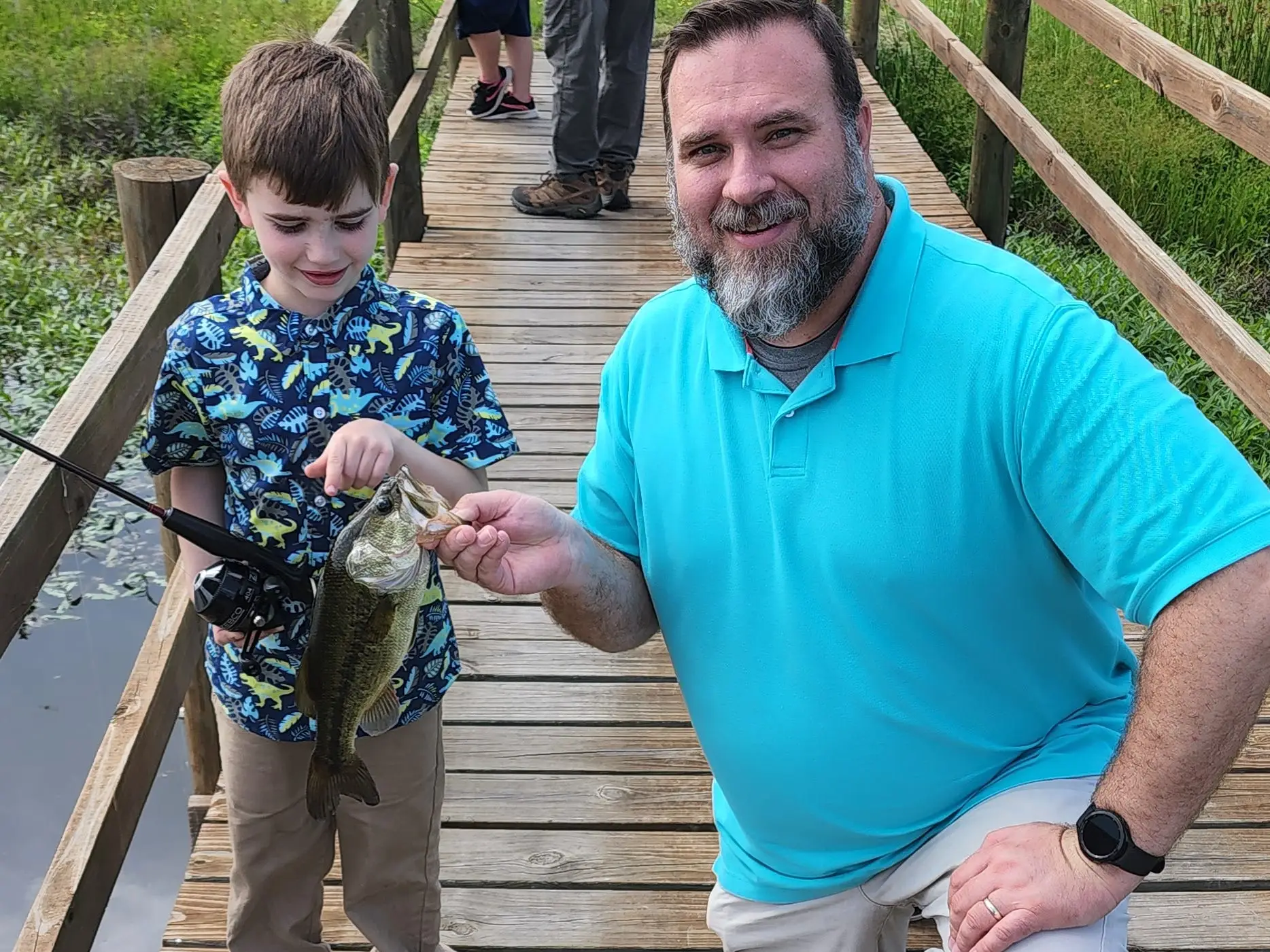An overweight man kneeling on a dock with a young boy