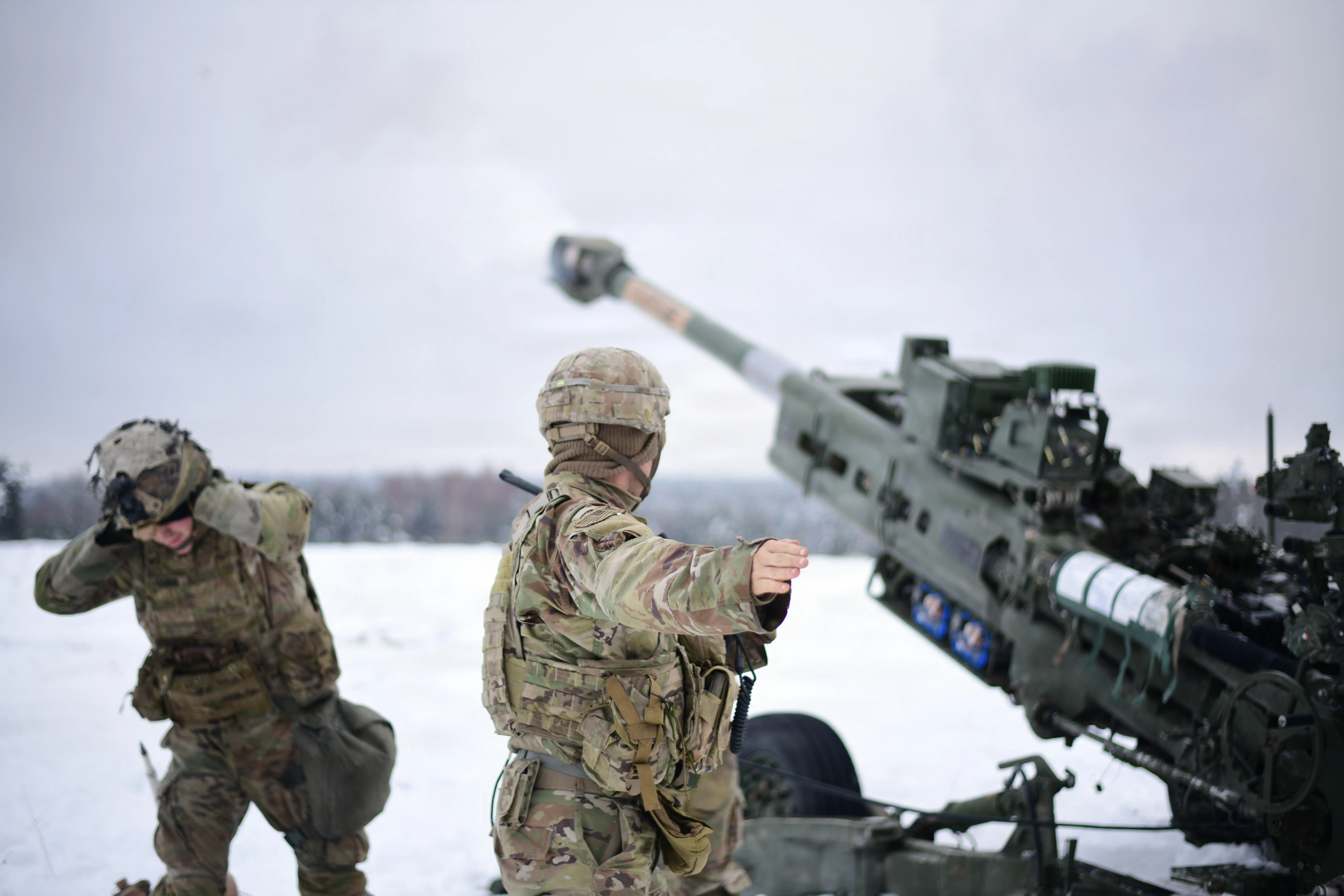 Two soldiers stand near an artillery piece about to fire in a wintry landscape.